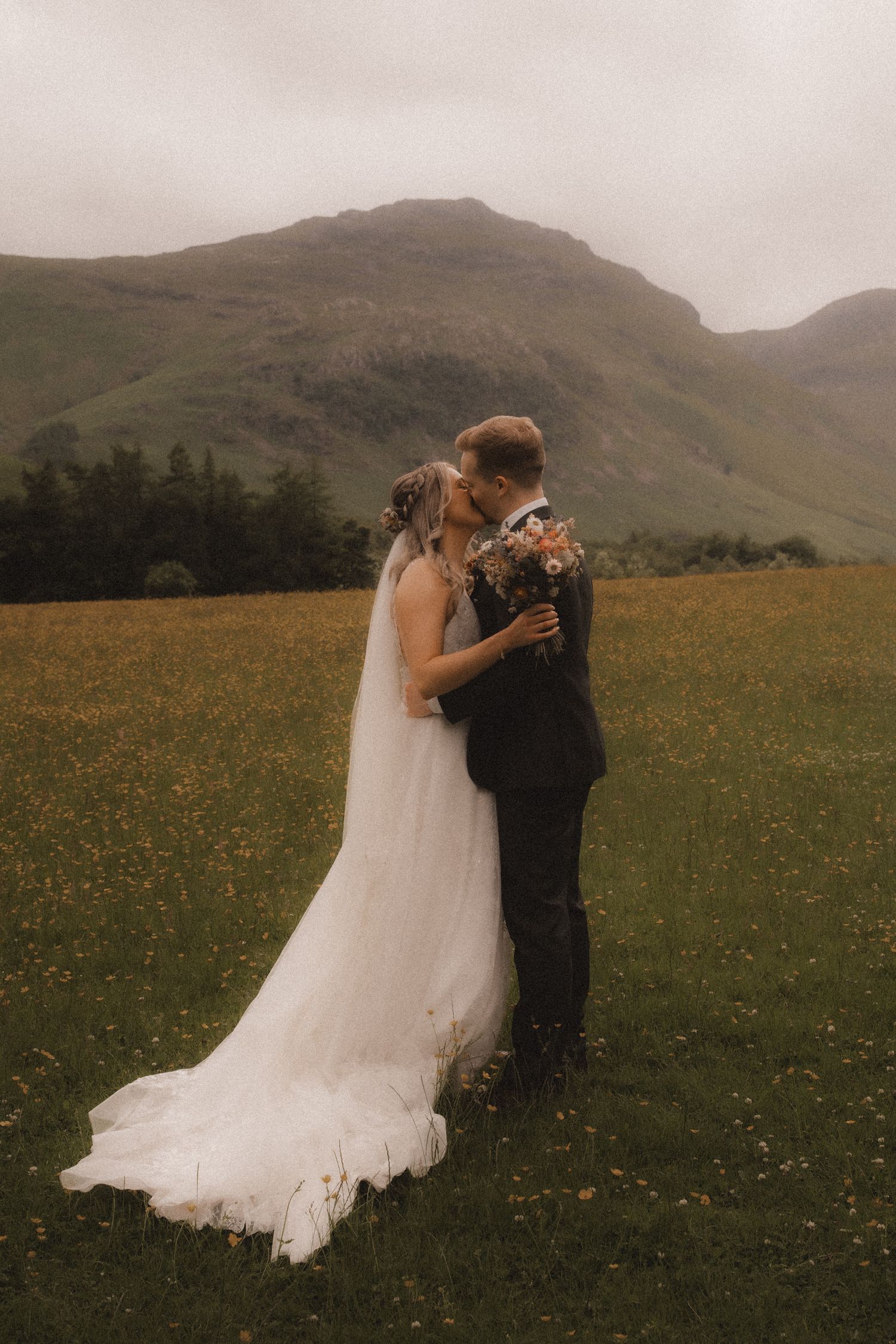 A couple embraces in a flowing white wedding dress and suit against the backdrop of misty Scottish highlands.