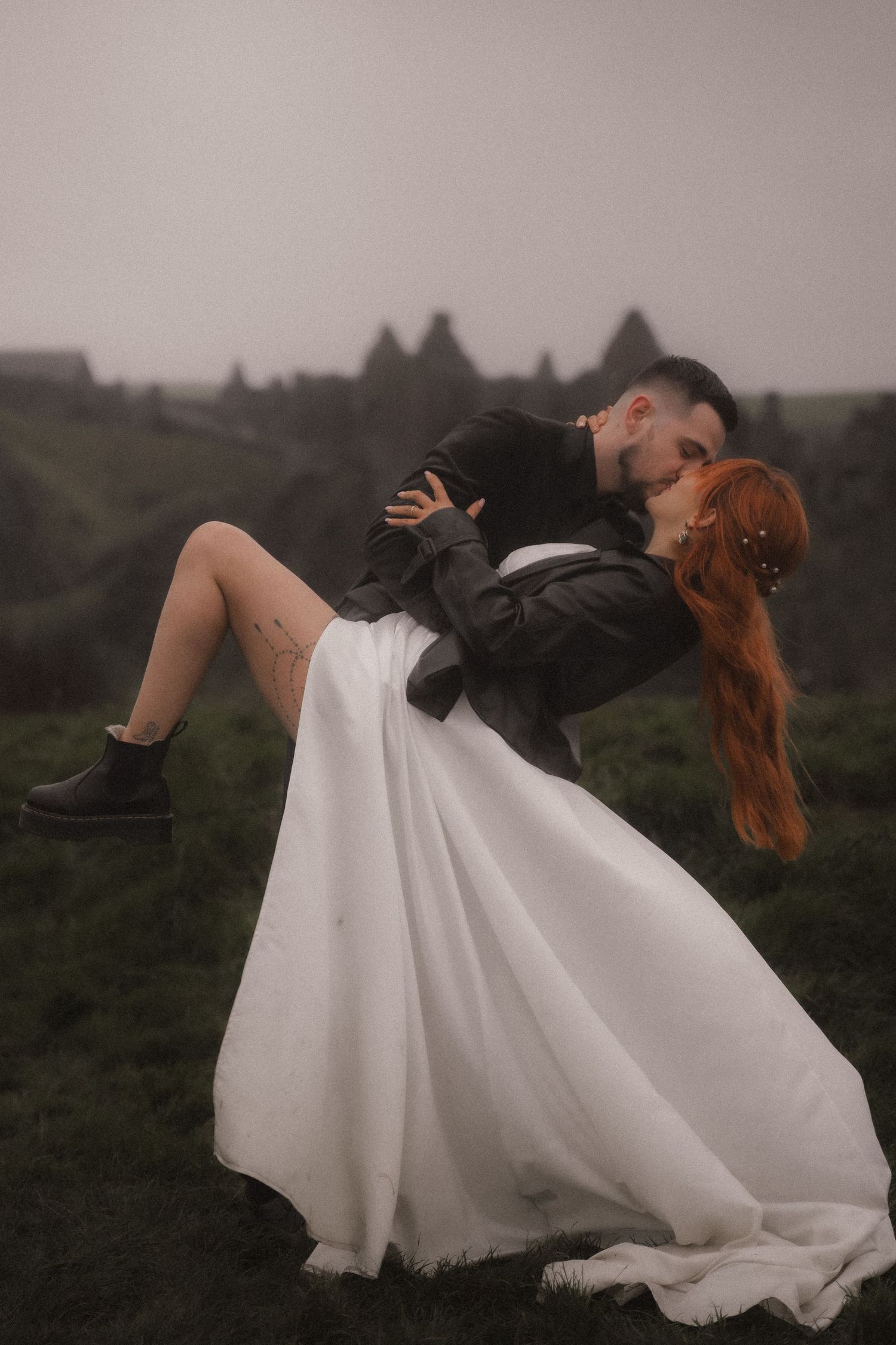 A dramatic wedding portrait showing a dip kiss pose against a moody mountainous landscape.