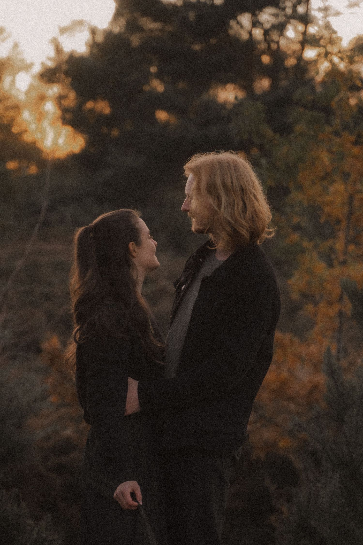 A romantic couple's portrait at sunset with golden bokeh through autumn trees in the background.