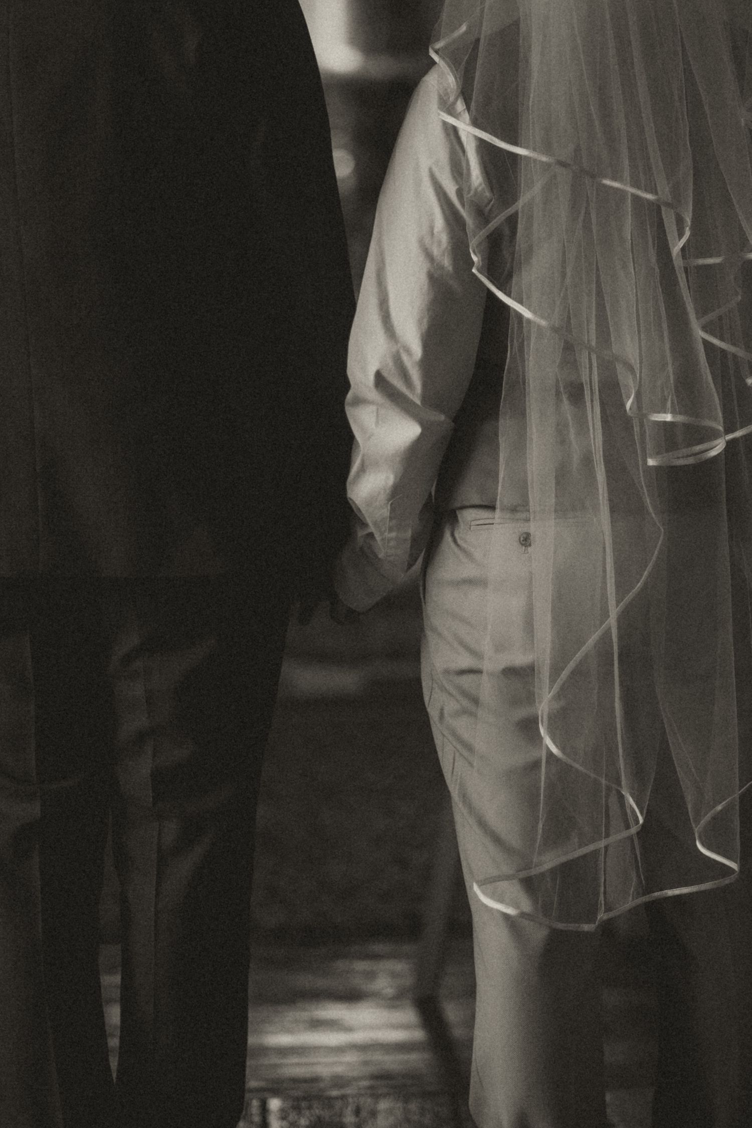 A black and white wedding photo showing the legs of wedding attendees with a bride's veil visible.