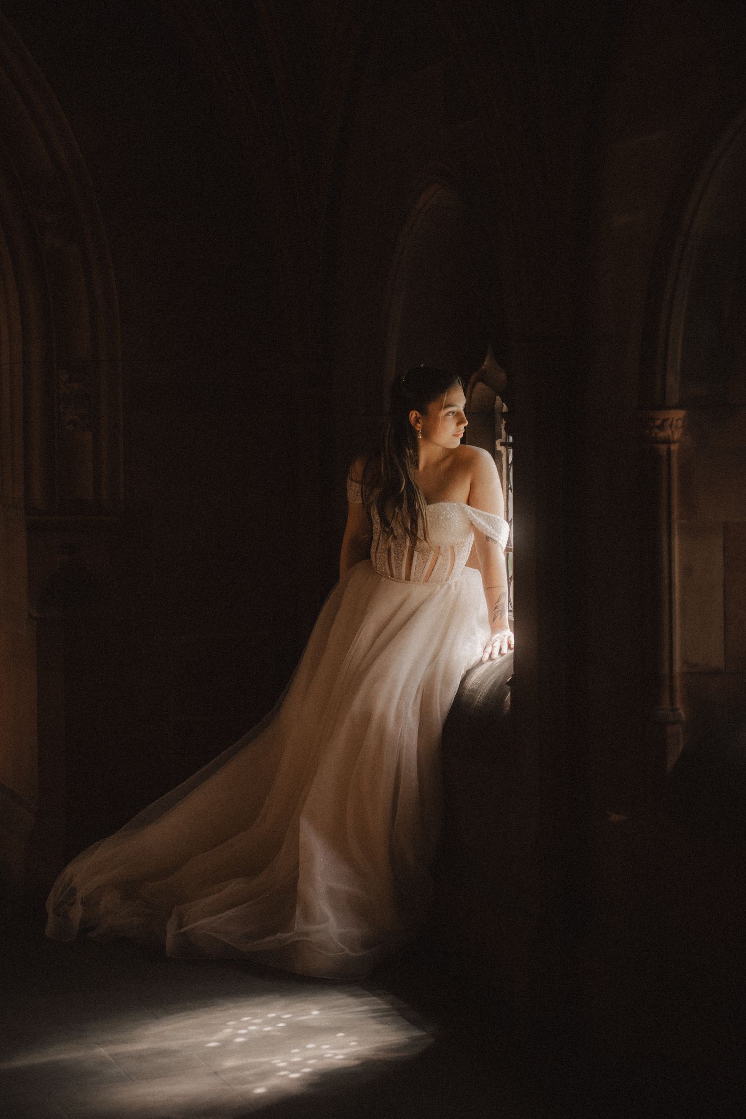 A bride in an elegant white wedding gown poses in dramatic lighting creating ethereal silhouettes against a dark background.