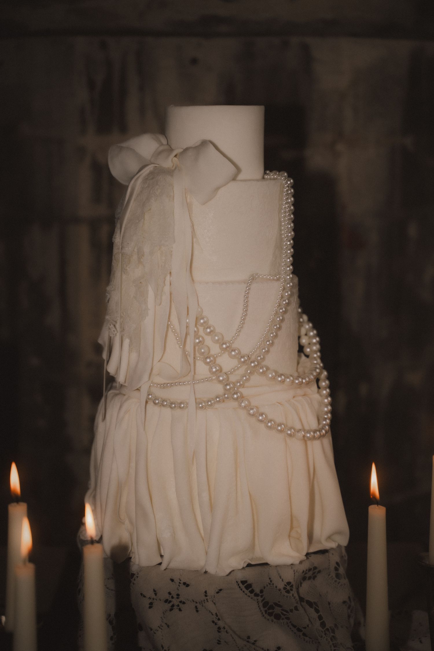 A white wedding dress with pearl necklaces is illuminated by candlelight in a dark, moody setting.