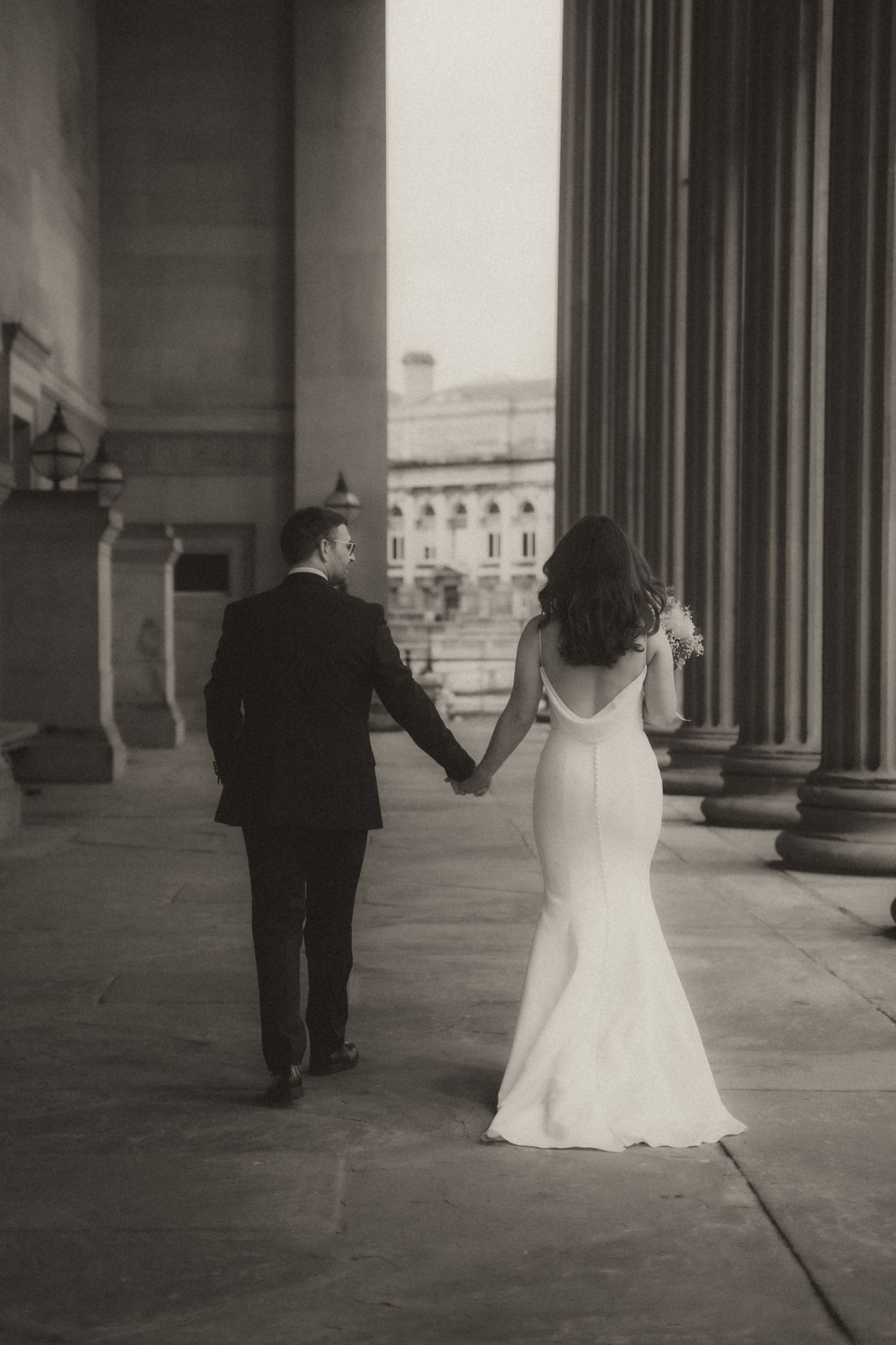 A black and white photo series shows a bride and groom walking away from the camera through a columned corridor.