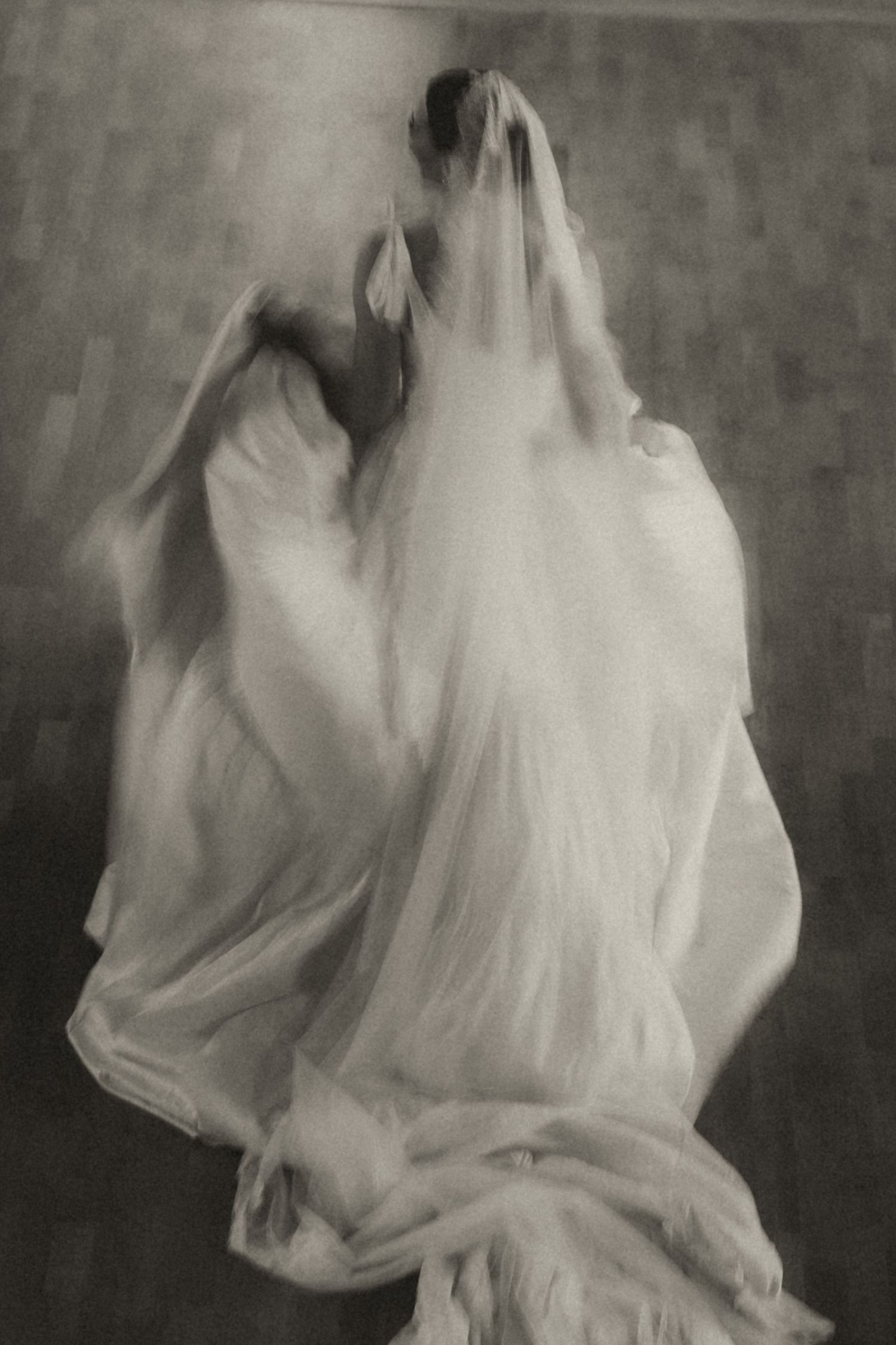A ghostly figure in flowing white fabric moves through a series of blurred, ethereal black and white photographs.