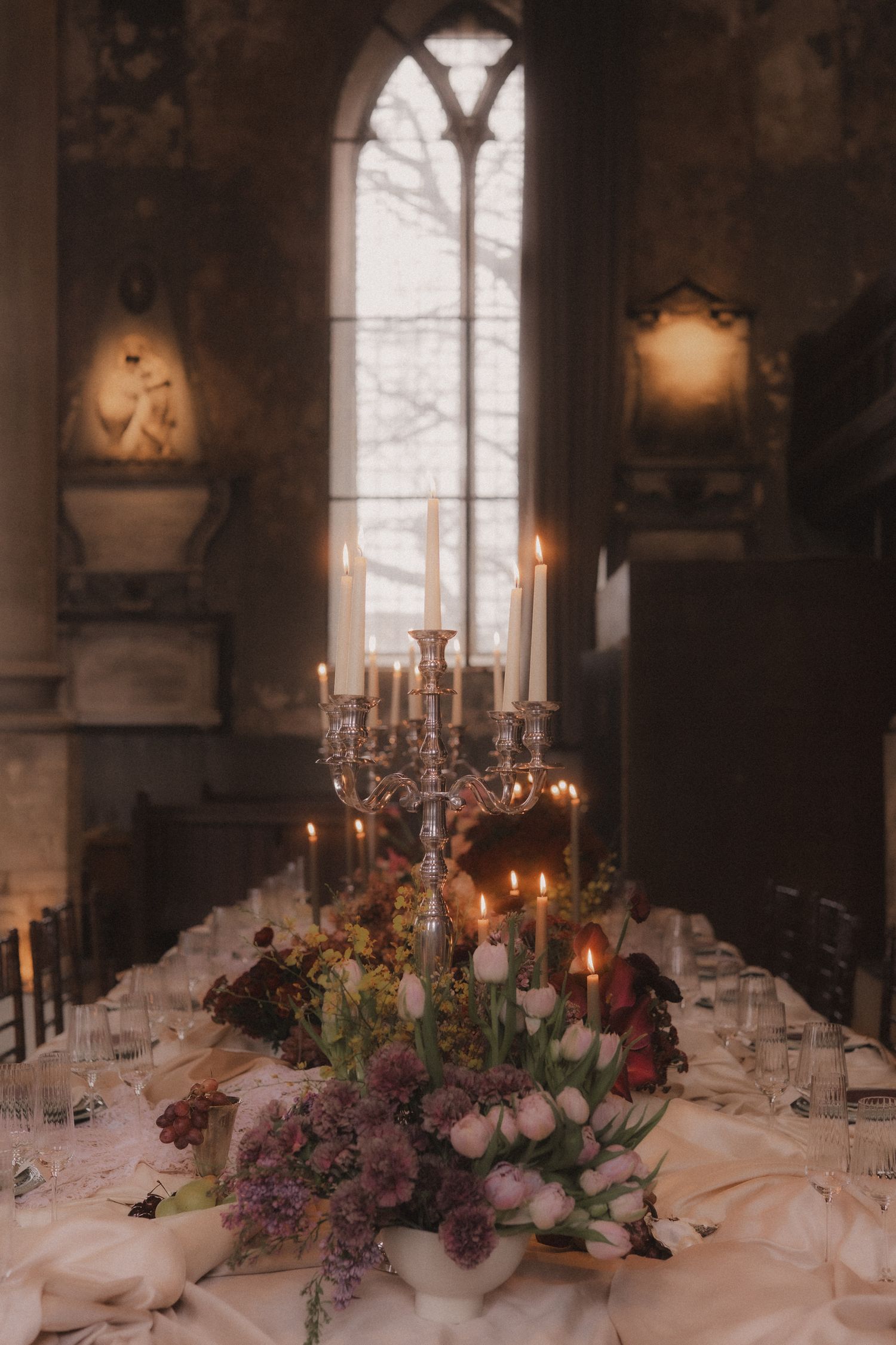 Elegant wedding reception table decorated with pink flowers, candelabras and romantic lighting in a historic venue.