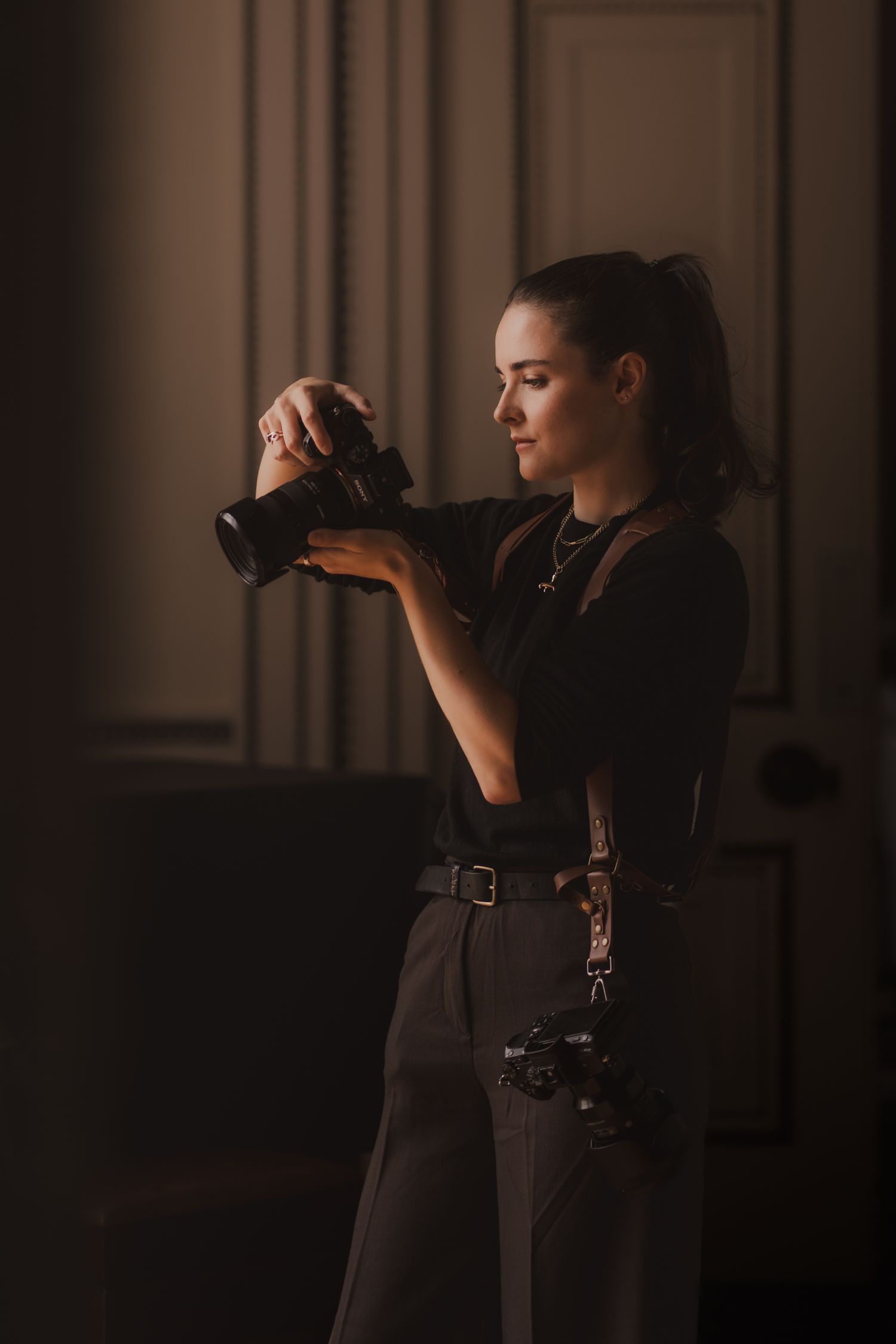 Photographer in black clothing works with camera in dimly lit studio space creating dramatic silhouette effects.