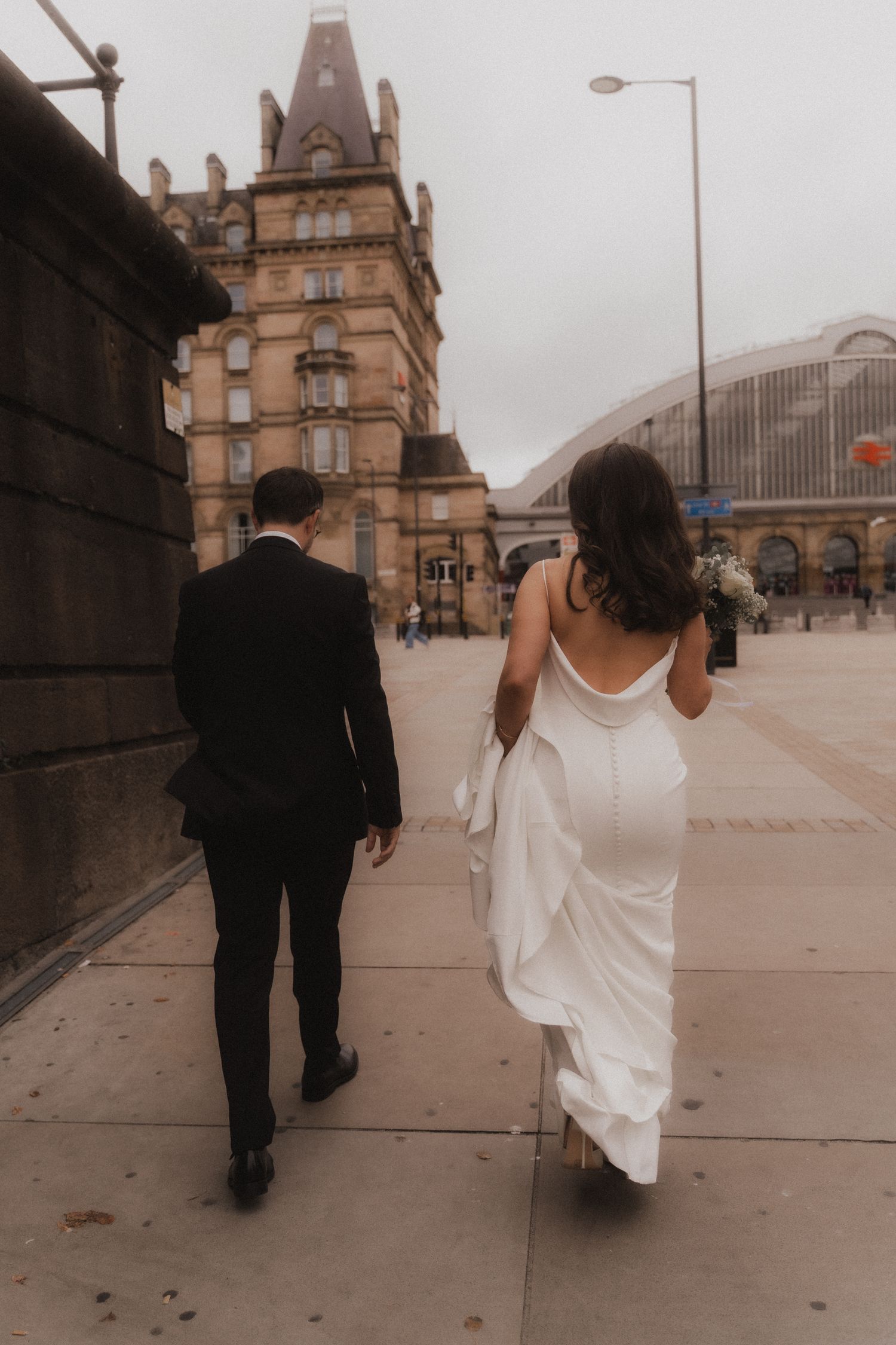 A couple in formal attire walks together along a historic building exterior in a series of romantic candid photos.