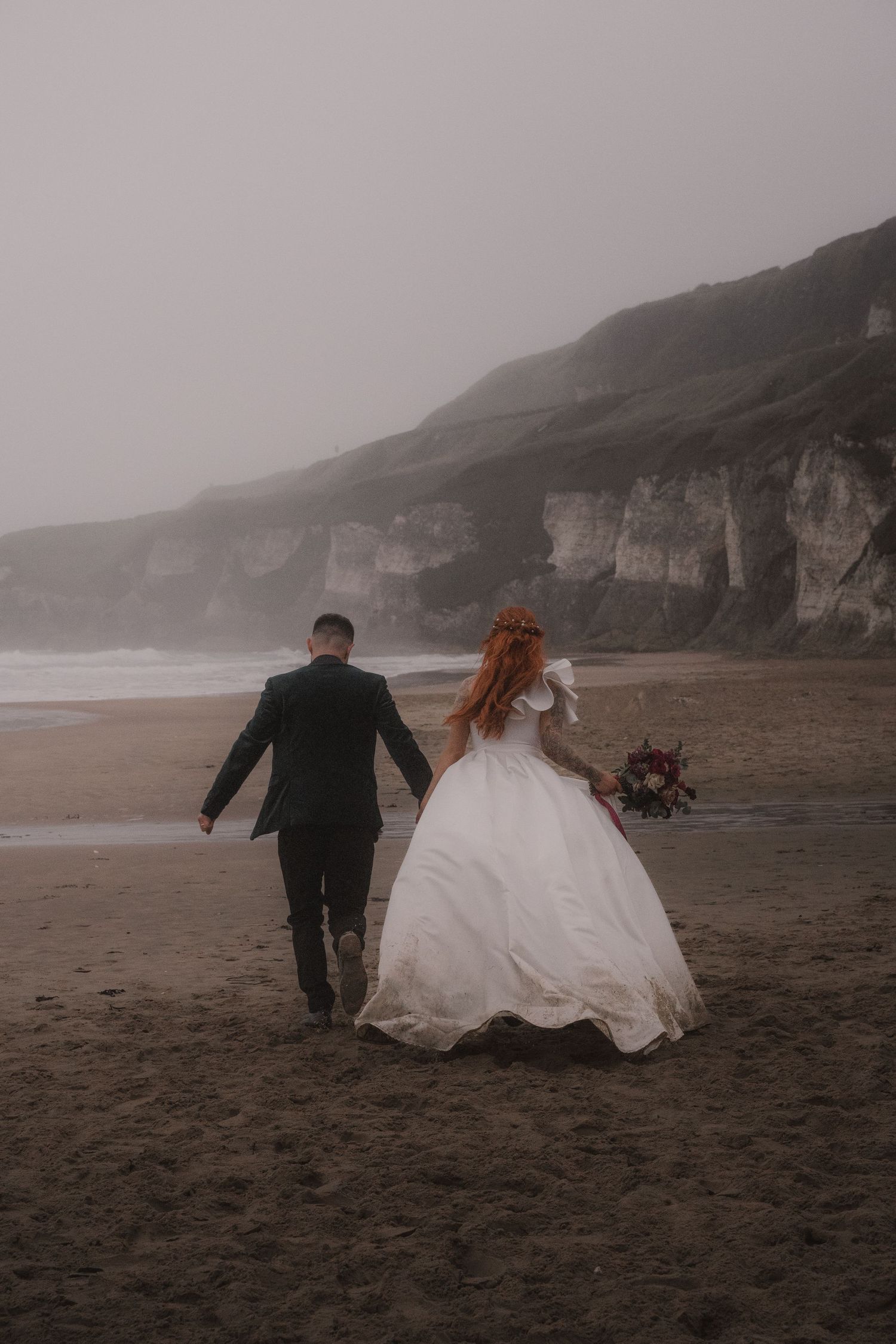 Couple walking along dramatic coastal cliffs on their wedding day.