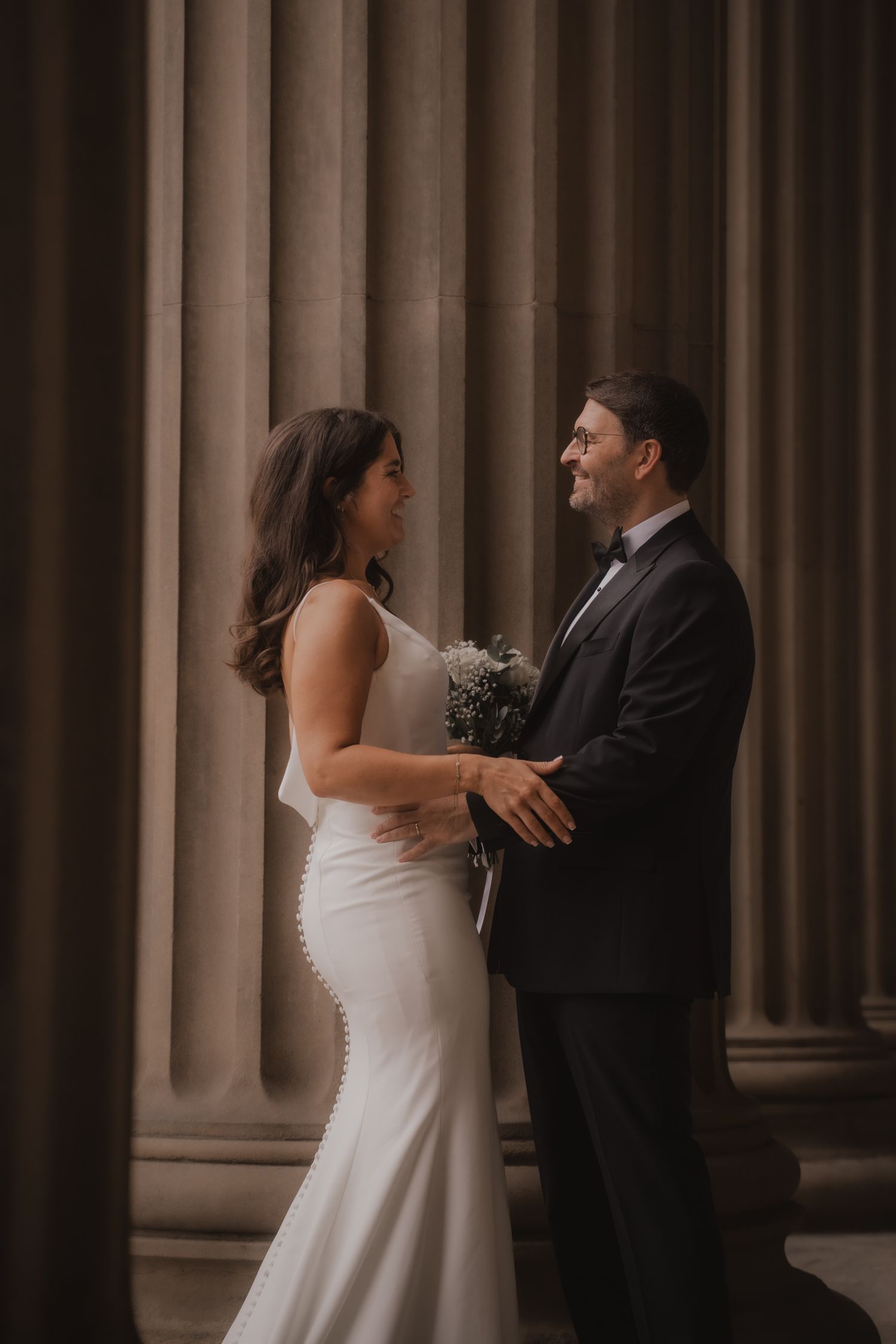 A couple shares a joyful moment together during their wedding ceremony in front of elegant stone columns.