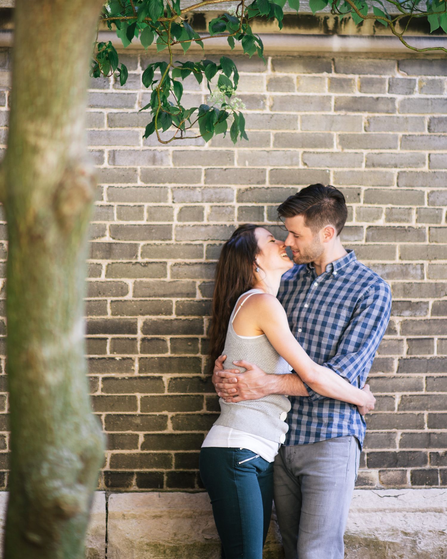 A couple shares romantic moments against a brick wall with green foliage in a series of intimate poses.
