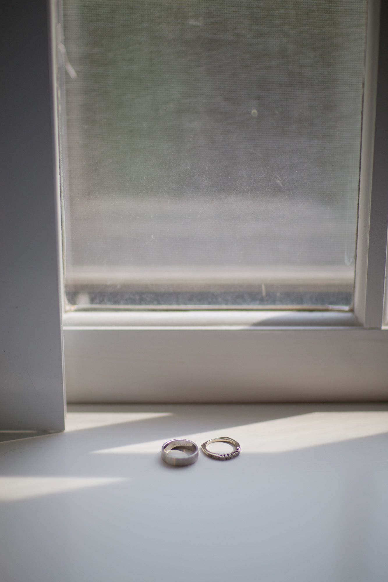 Two wedding rings casting shadows on a white windowsill in natural light.