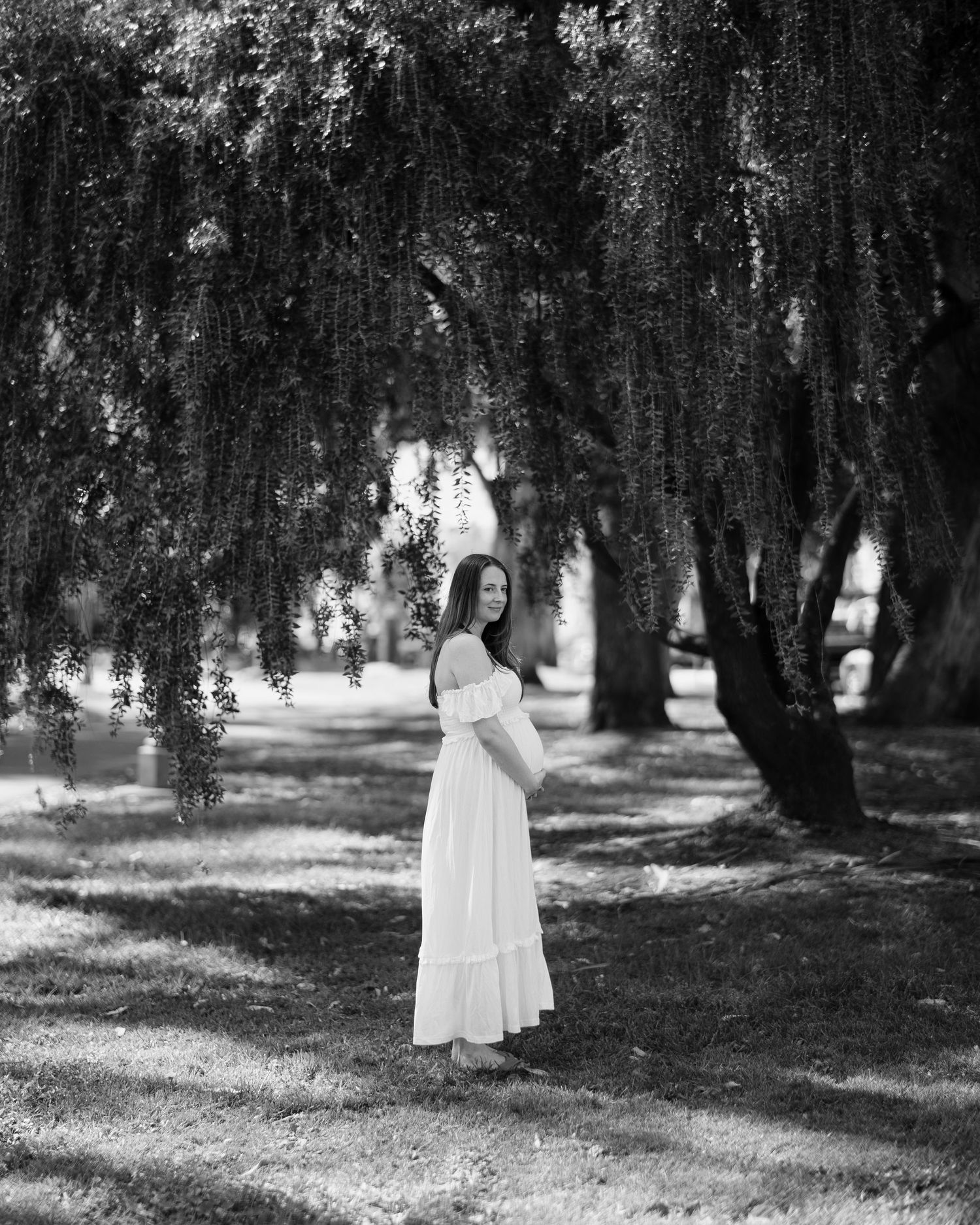 A person in a white dress stands among mossy trees in a dreamy black and white forest setting.