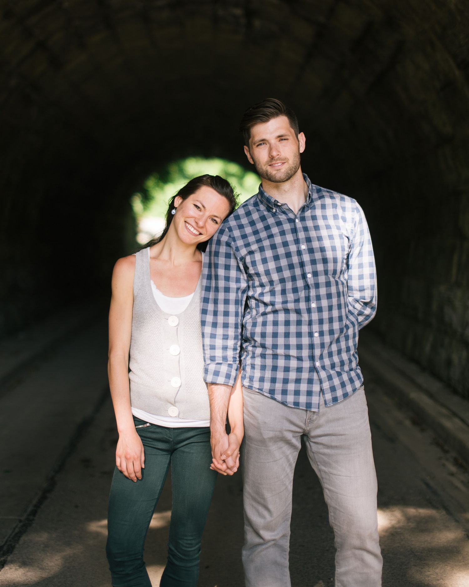 Couple walking and holding hands in a shaded outdoor setting wearing casual attire.