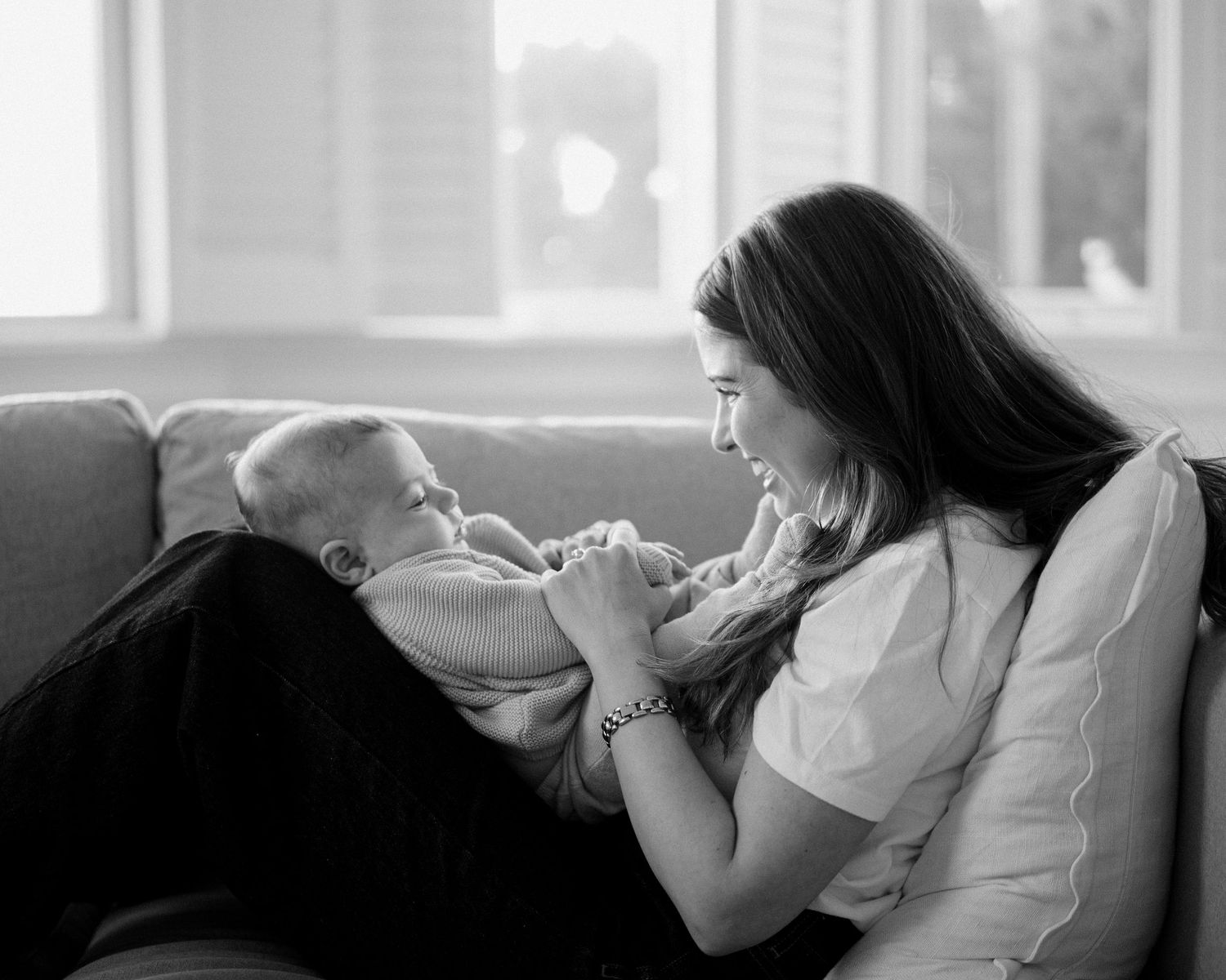 Black and white photo of a young mother tenderly holding her newborn baby on a cozy sofa.