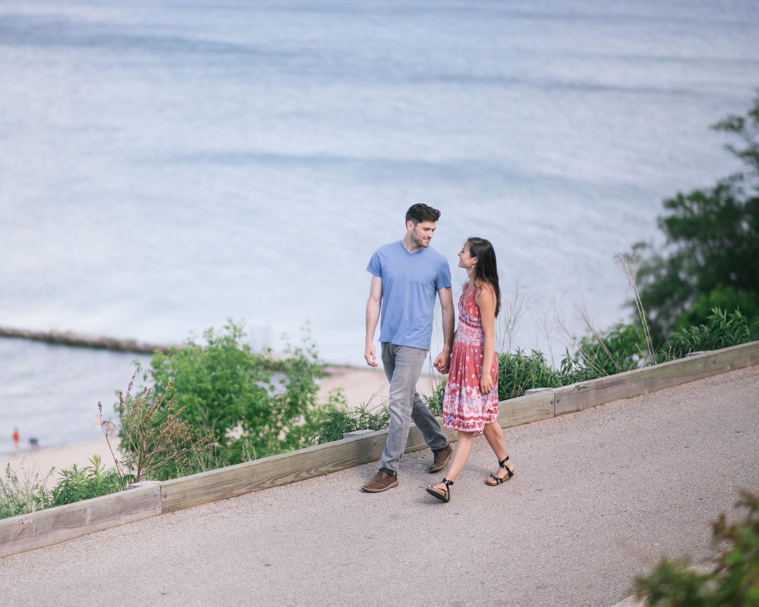 A couple walking along a seaside path on a sunny day with ocean views in the background.