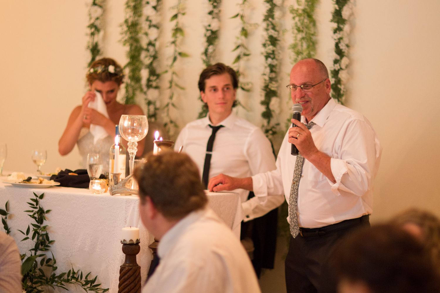 Wedding guests enjoy dinner and conversation at elegantly decorated reception tables with hanging greenery.