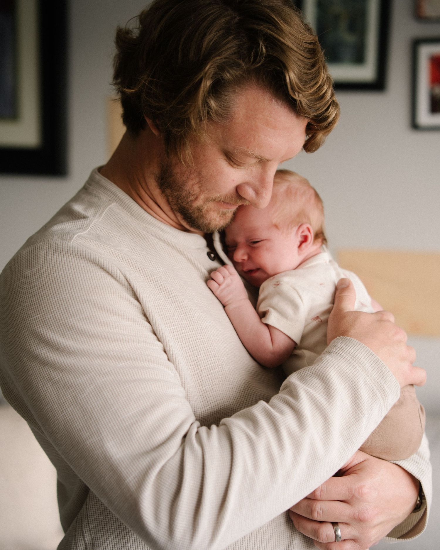 A tender moment as an adult in a beige sweater cradles and snuggles with a sleeping newborn baby.