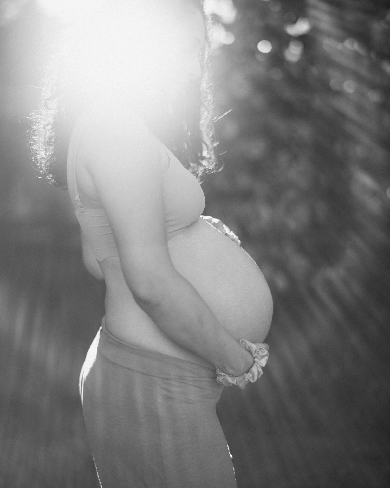 A black and white silhouetted maternity photo shows an expectant mother's profile in soft natural sunlight.