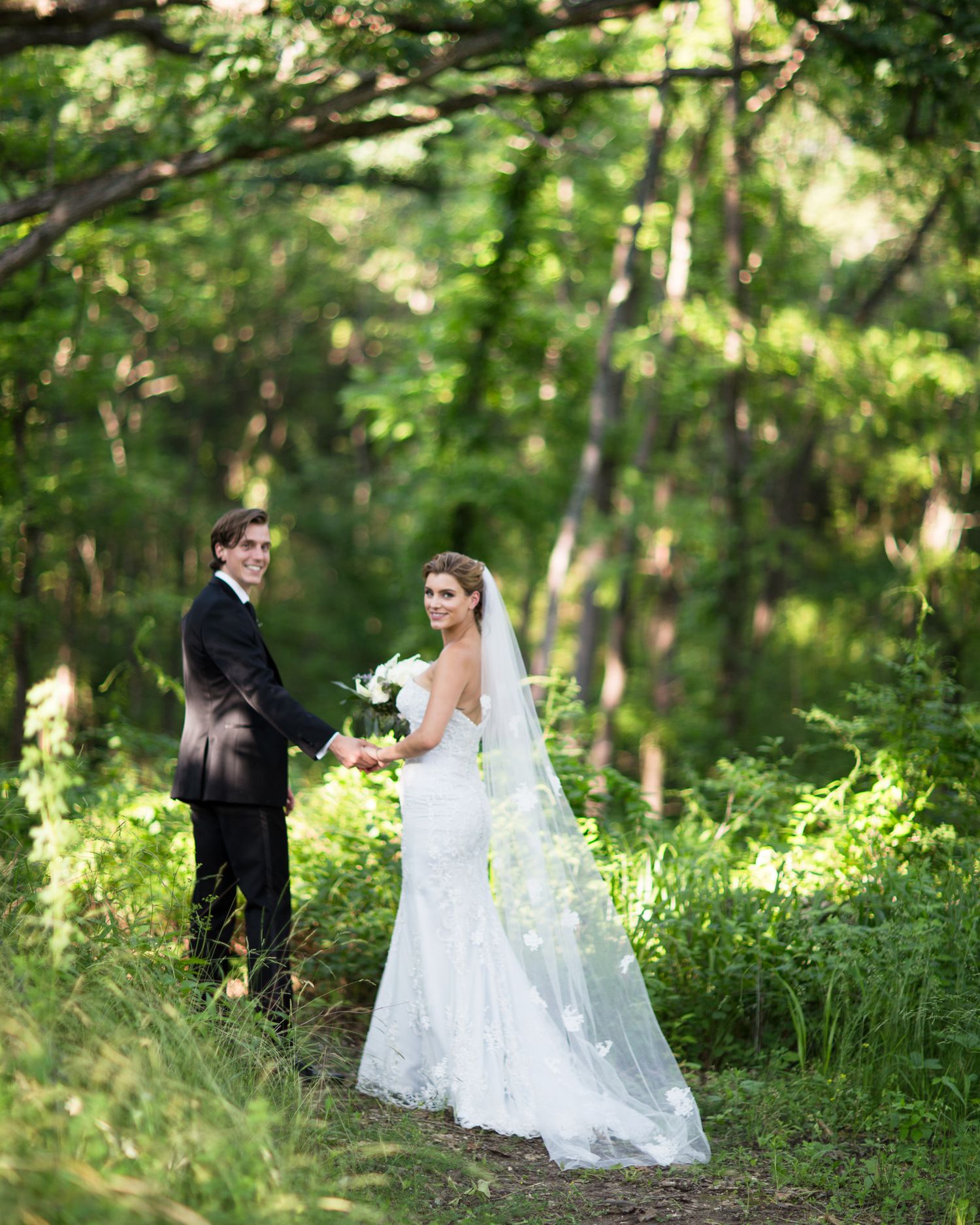 A couple shares a romantic moment in a lush green forest setting during their wedding photoshoot.