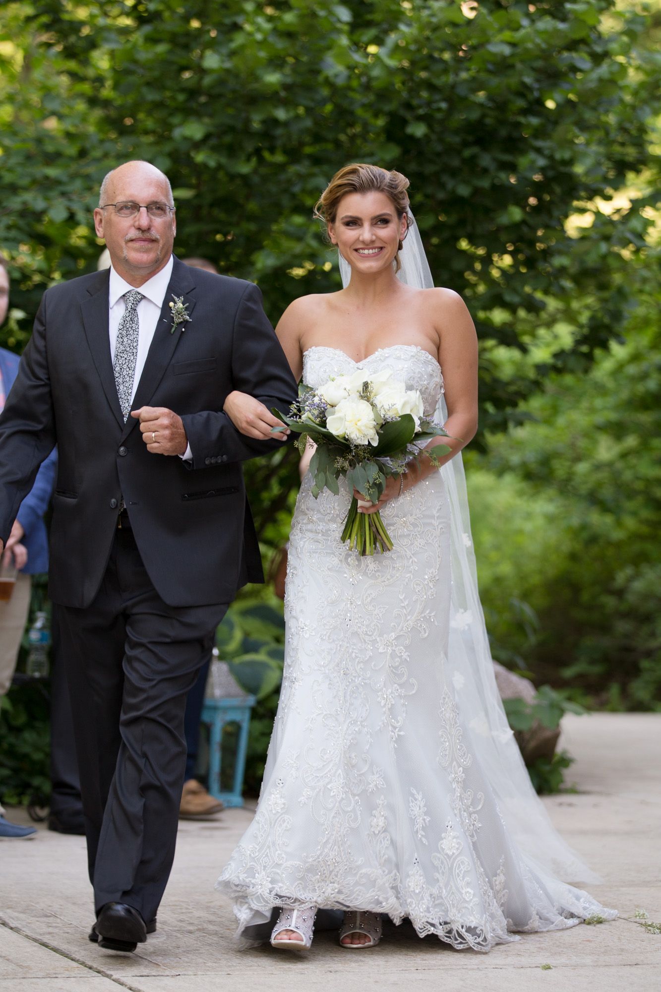A wedding processional in a garden setting with white floral bouquets and formal attire.