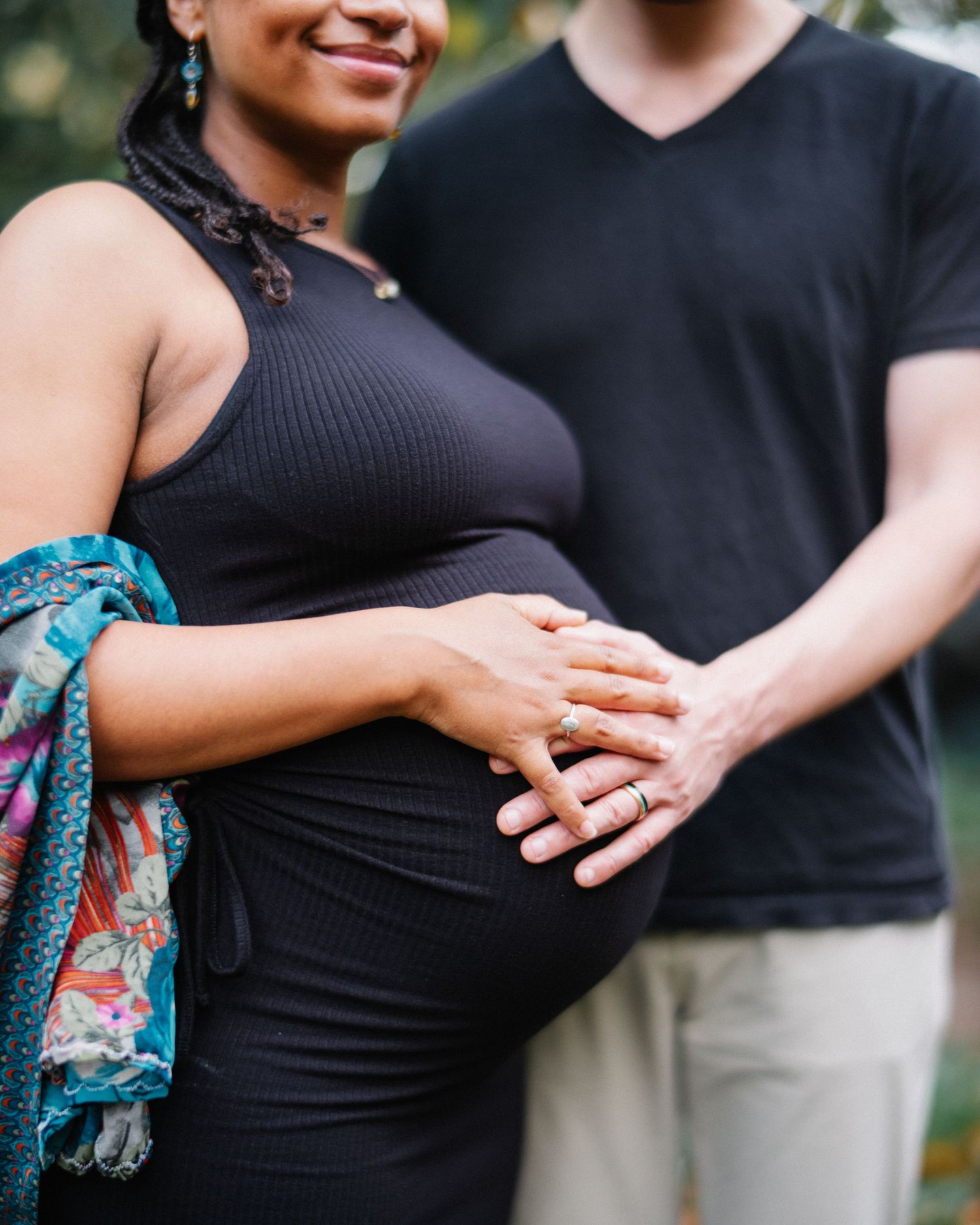 A couple wearing black outfits holds hands and shows off an engagement ring in a romantic outdoor photoshoot.