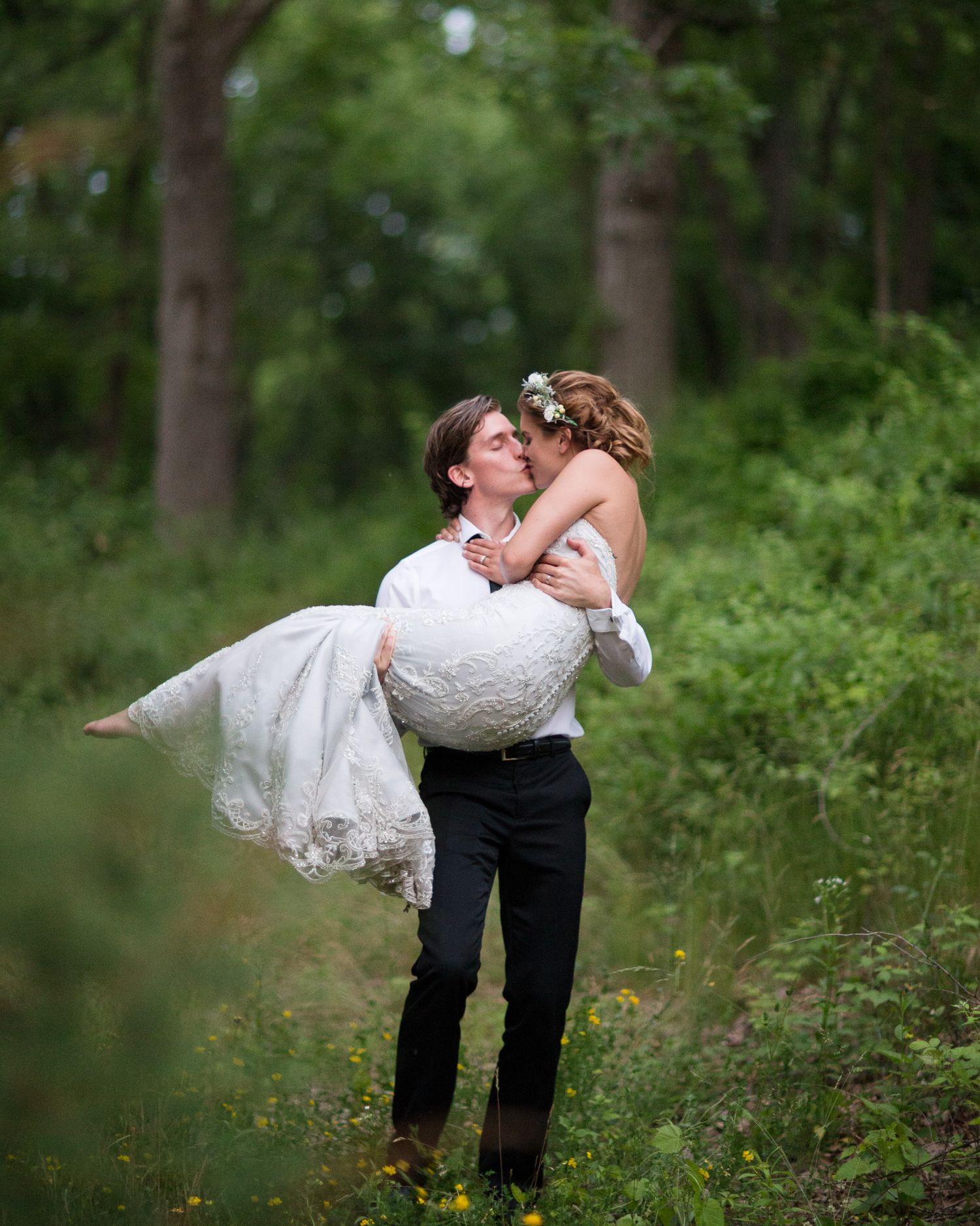 A romantic dip kiss between newlyweds in a lush green forest setting.