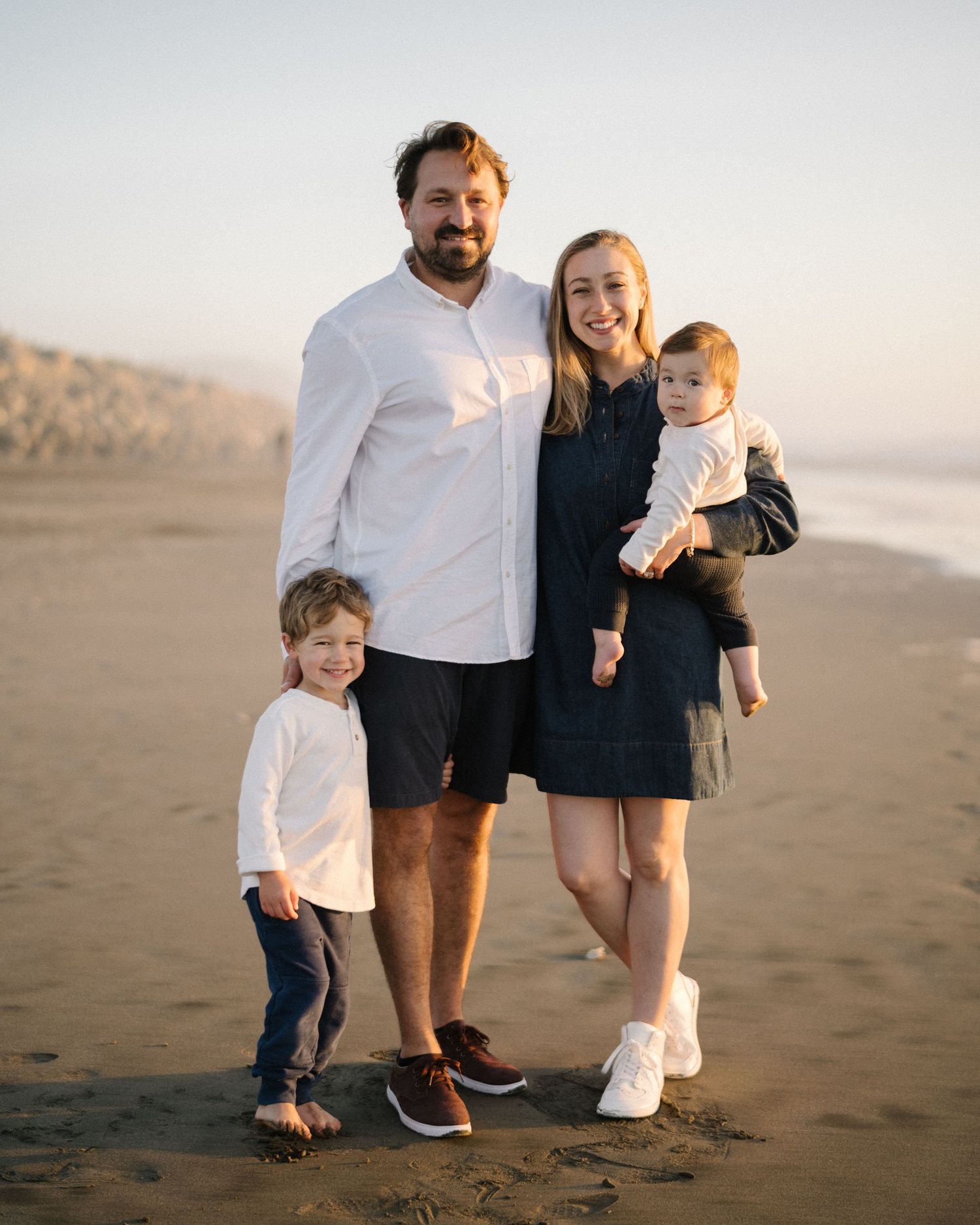 Family enjoying a casual moment together on a sandy beach at sunset.