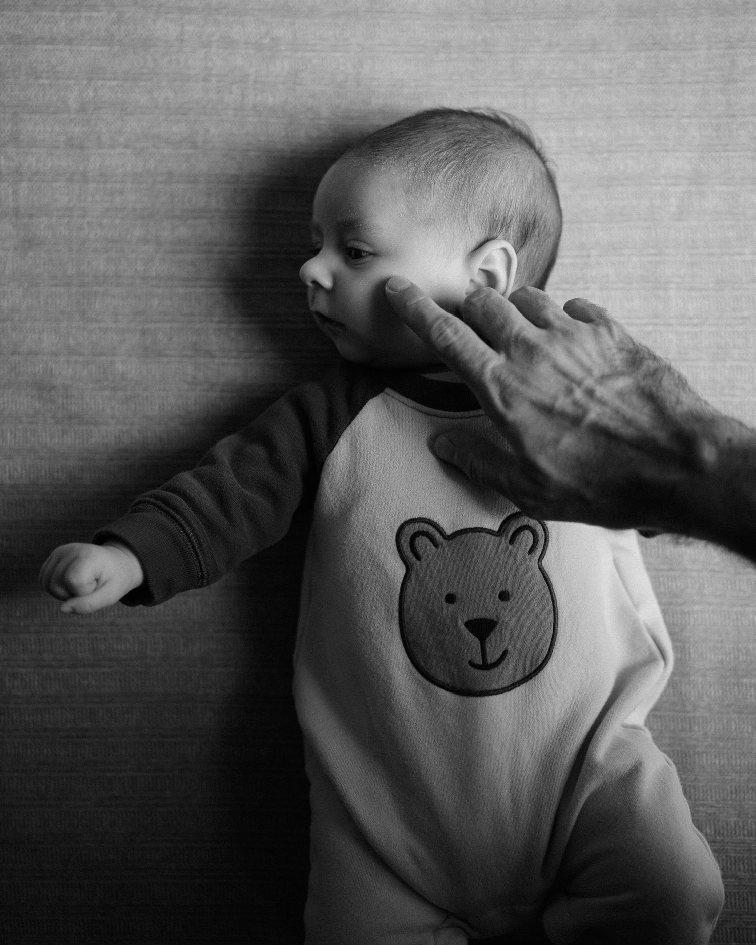 A series of black and white photos showing a baby wearing a teddy bear onesie lying on a blanket.
