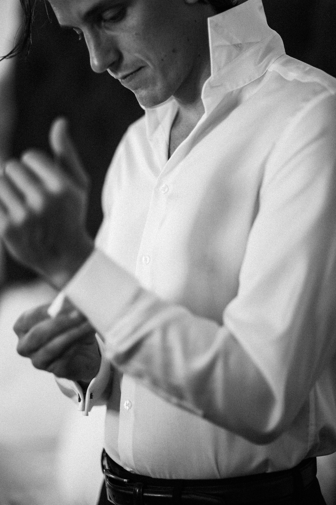 A black and white sequence showing someone buttoning up a white dress shirt sleeve.