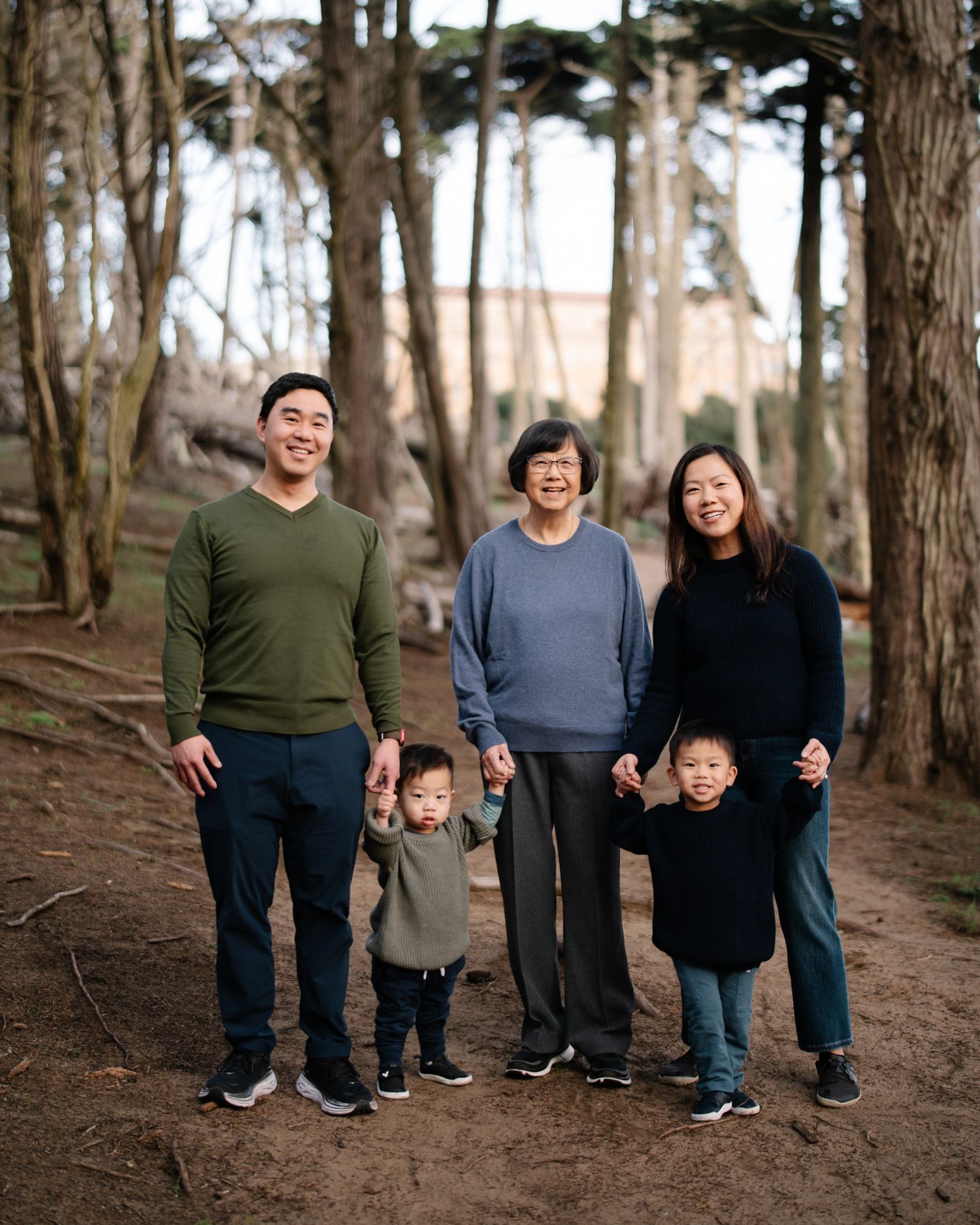 A family group stands together among tall pine trees in a forest setting during an outdoor photo session.