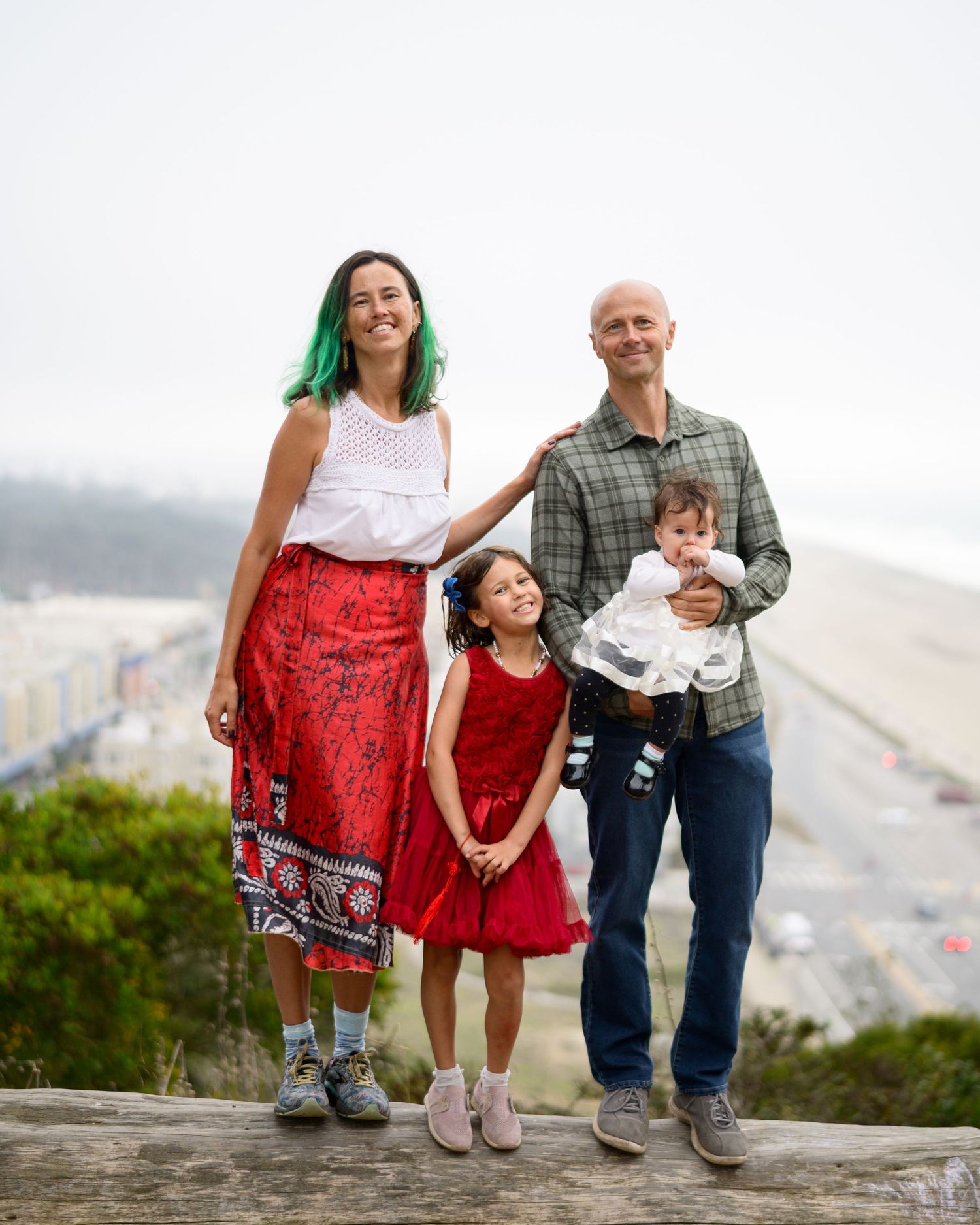Family of four posing outdoors at a scenic beach overlook, smiling together on a sunny day.