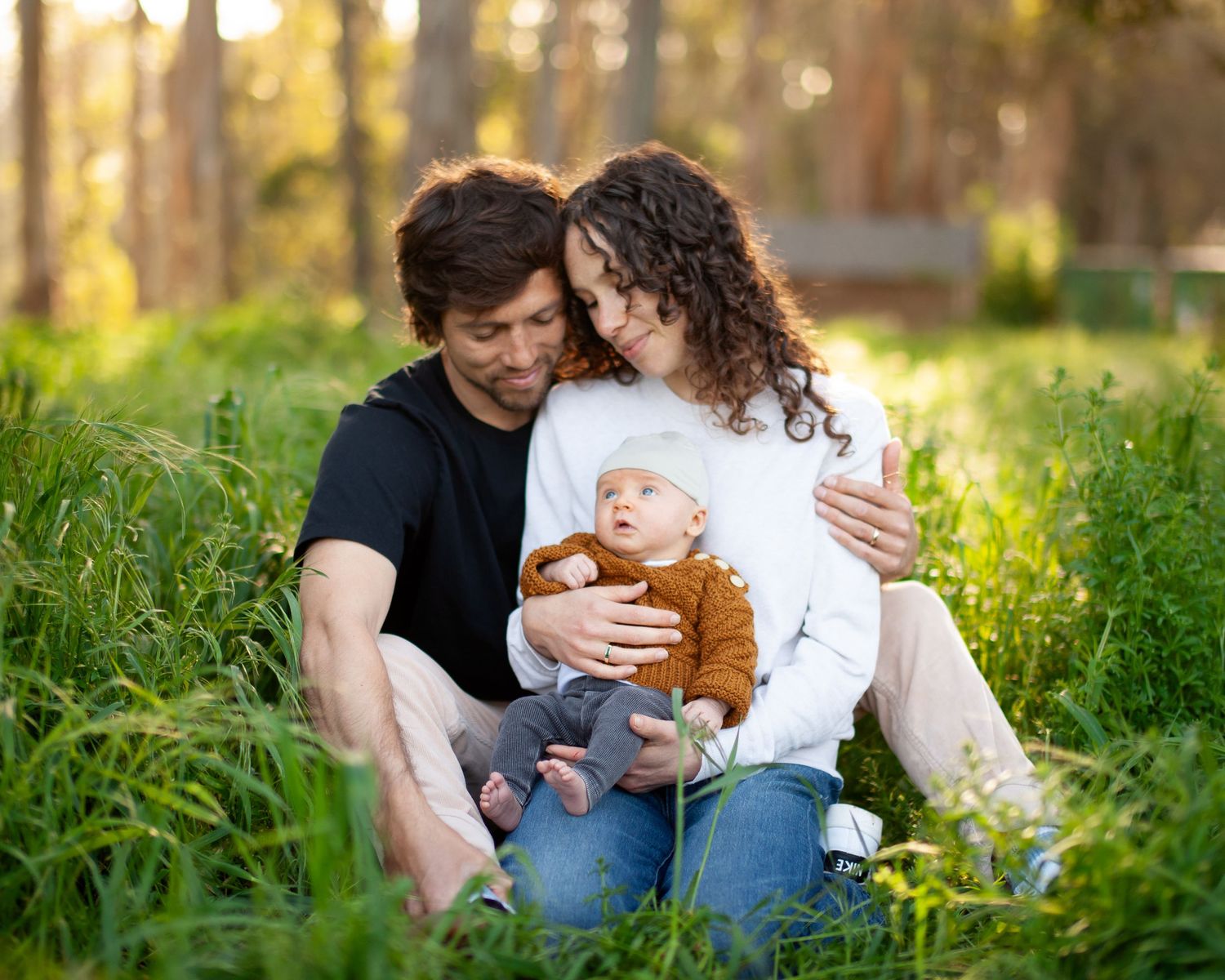 Family sitting together on grass in golden sunlight during outdoor photo session at sunset.