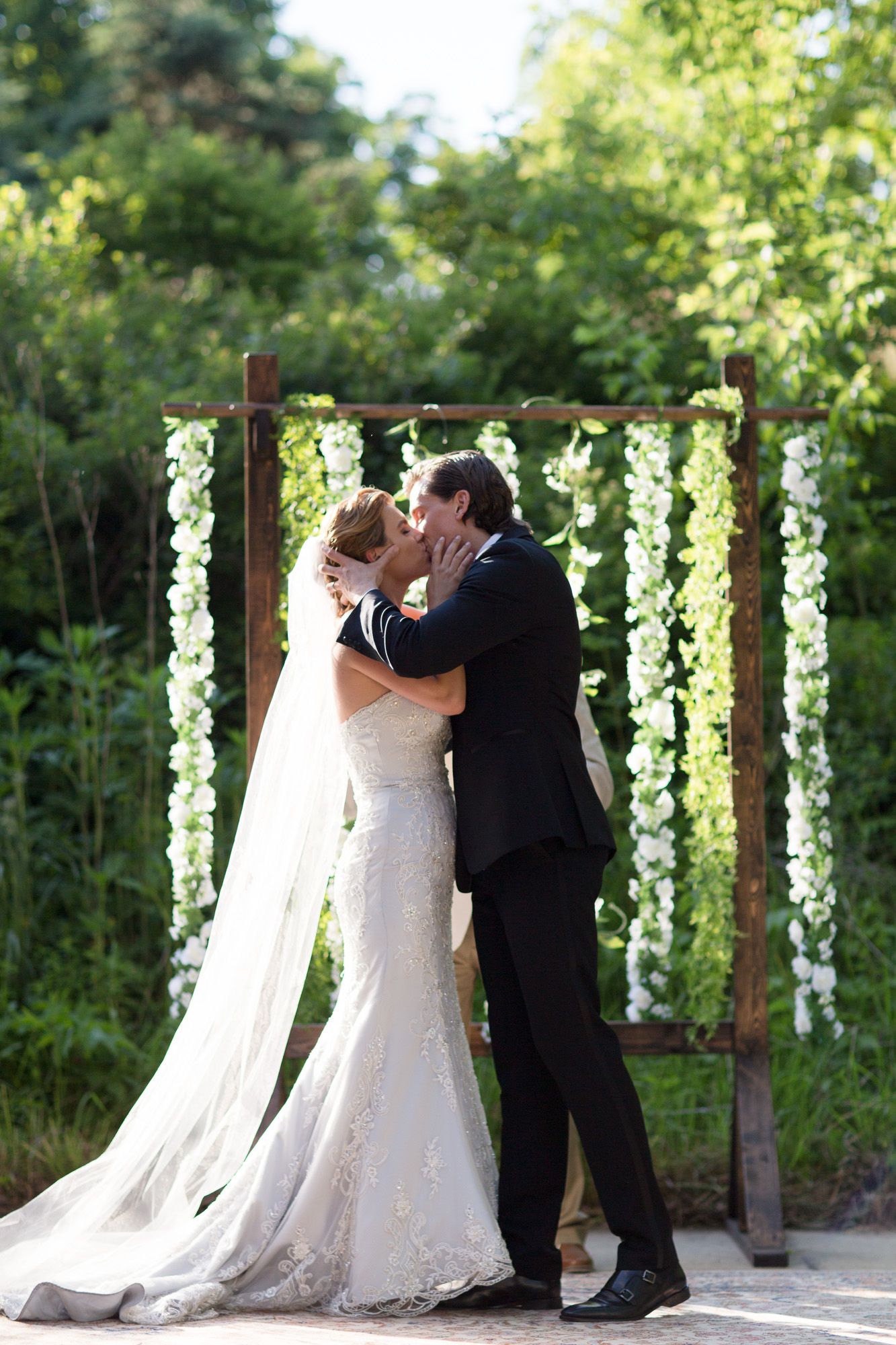 Wedding ceremony under hanging floral decorations with couple sharing their first kiss.