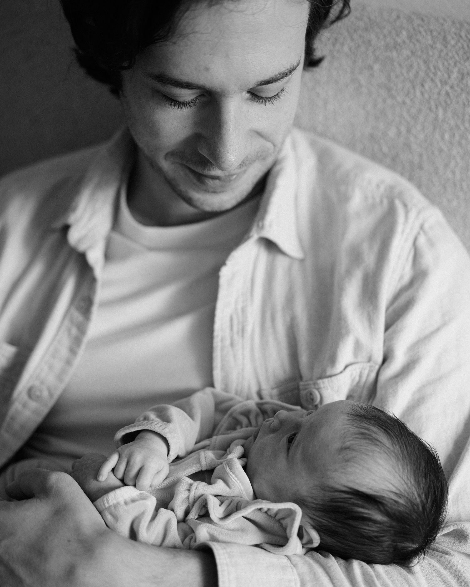 Black and white photo of a young man smiling down at a newborn baby cradled in his arms.