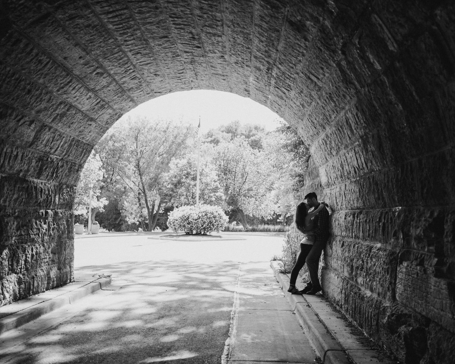 A black and white panoramic sequence showing a person walking through a stone tunnel archway.