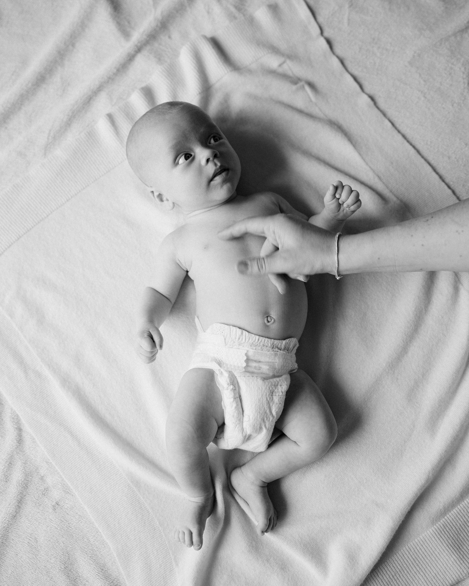 A series of black and white photographs showing a sleeping baby in different positions on white bedding.
