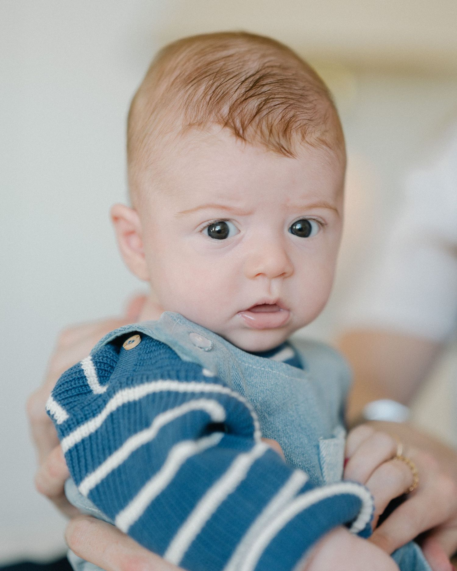A baby wearing a blue and white striped bib looks at the camera with wide eyes and an adorable expression.