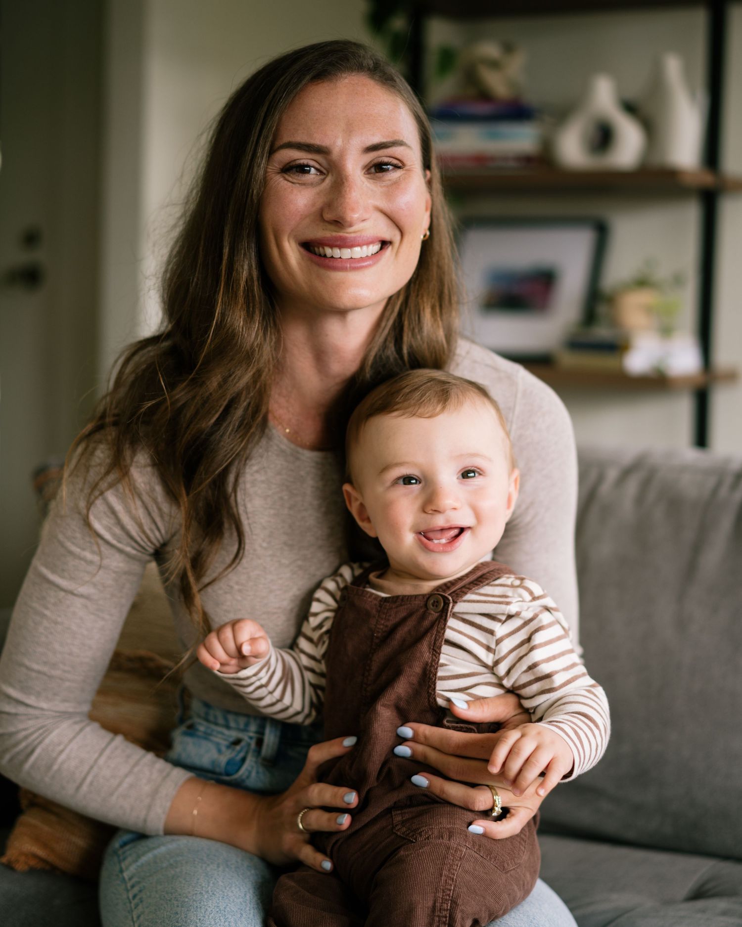A mother and baby share joyful moments together while sitting on a couch in a living room.