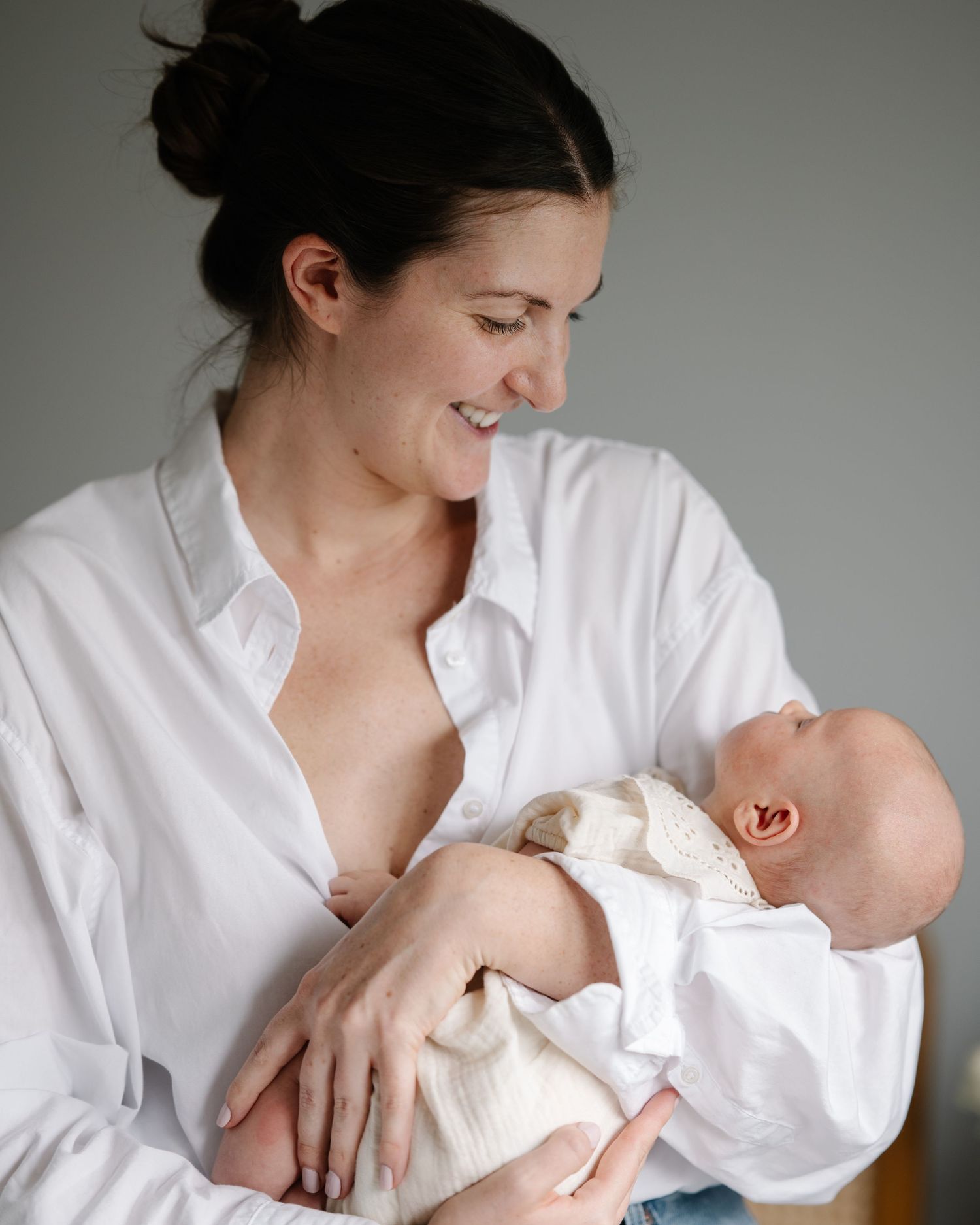 A smiling mother in a white shirt breastfeeding her newborn baby, sharing a tender bonding moment.