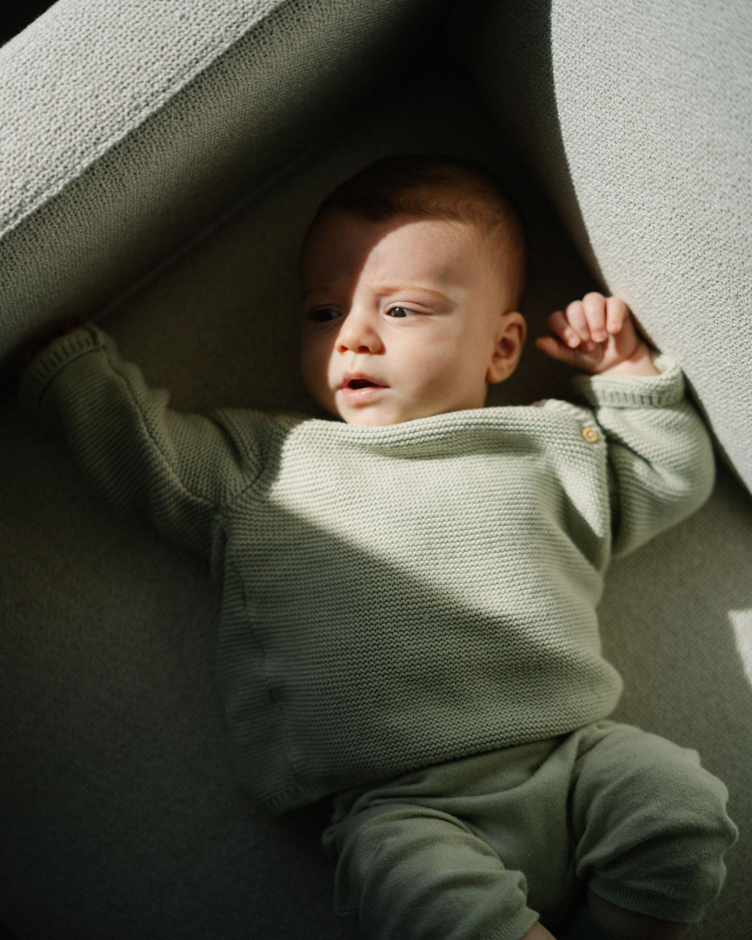 Person wearing an olive green turtleneck sweater photographed in dramatic shadows against a light background.