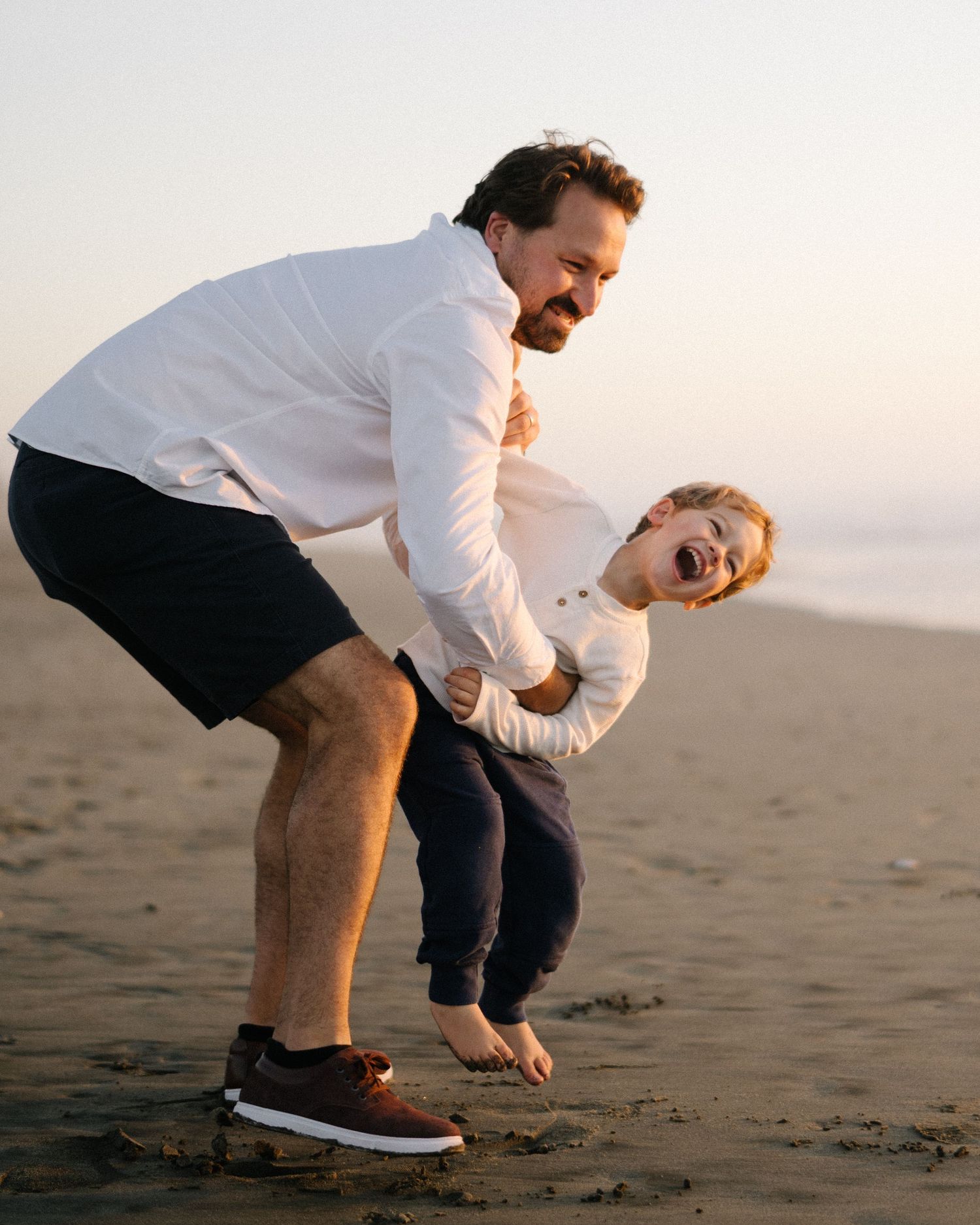 Adults crouch down and play in the sand at sunset on the beach.