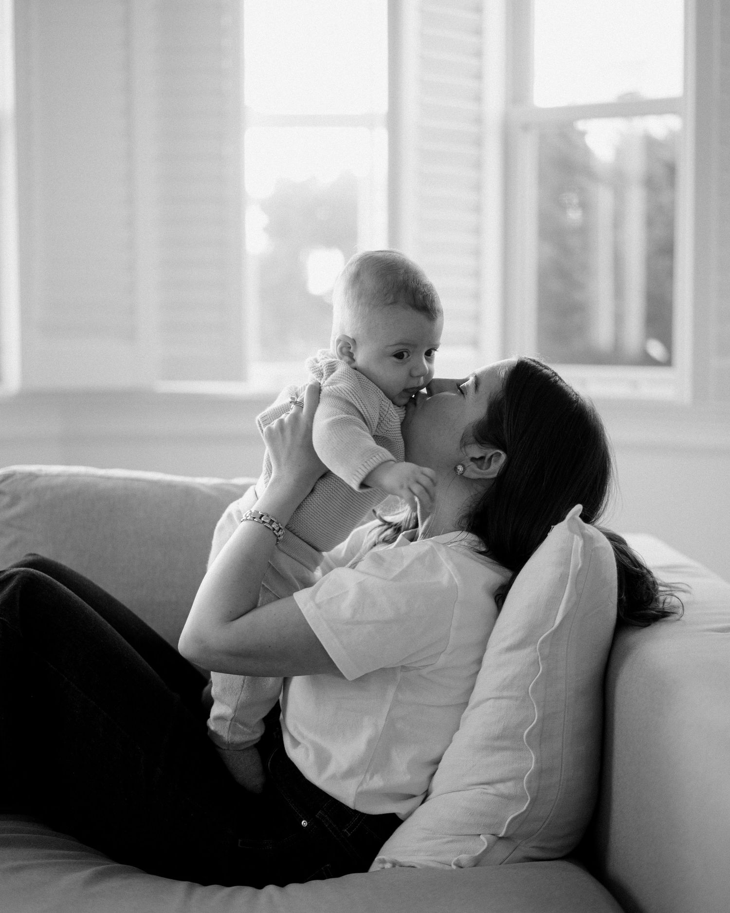 A tender black and white photo series showing intimate bonding moments between a parent and baby on a couch.
