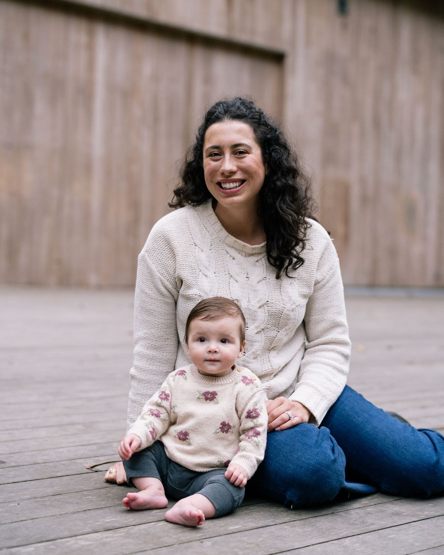 A sequence of candid moments shows a baby sitting on wooden decking while wearing a cream-colored sweater.