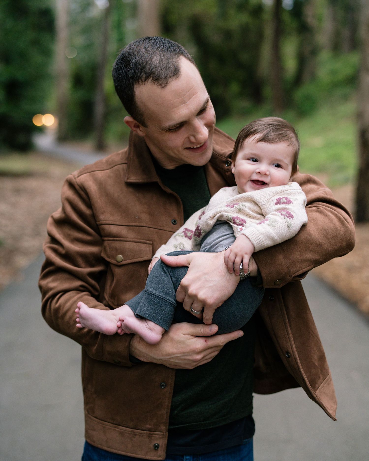A tender moment shared between parent and baby on a wooded path while wearing a brown leather jacket.