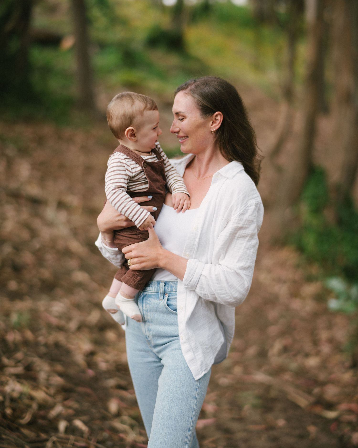 A parent and child share tender moments together in a wooded outdoor setting wearing casual clothing.