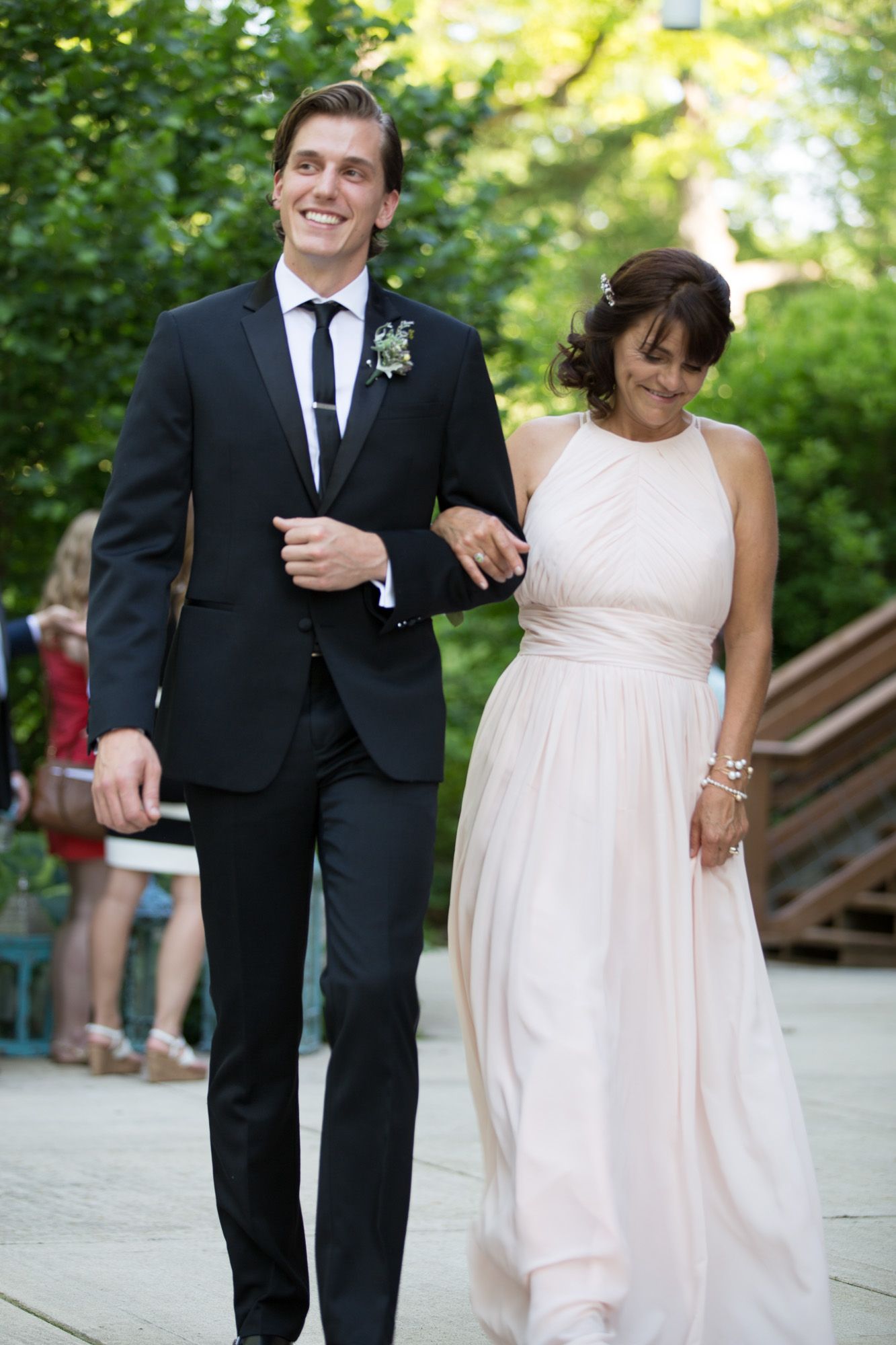 Wedding party members in formal attire walking together outdoors on a sunny day.