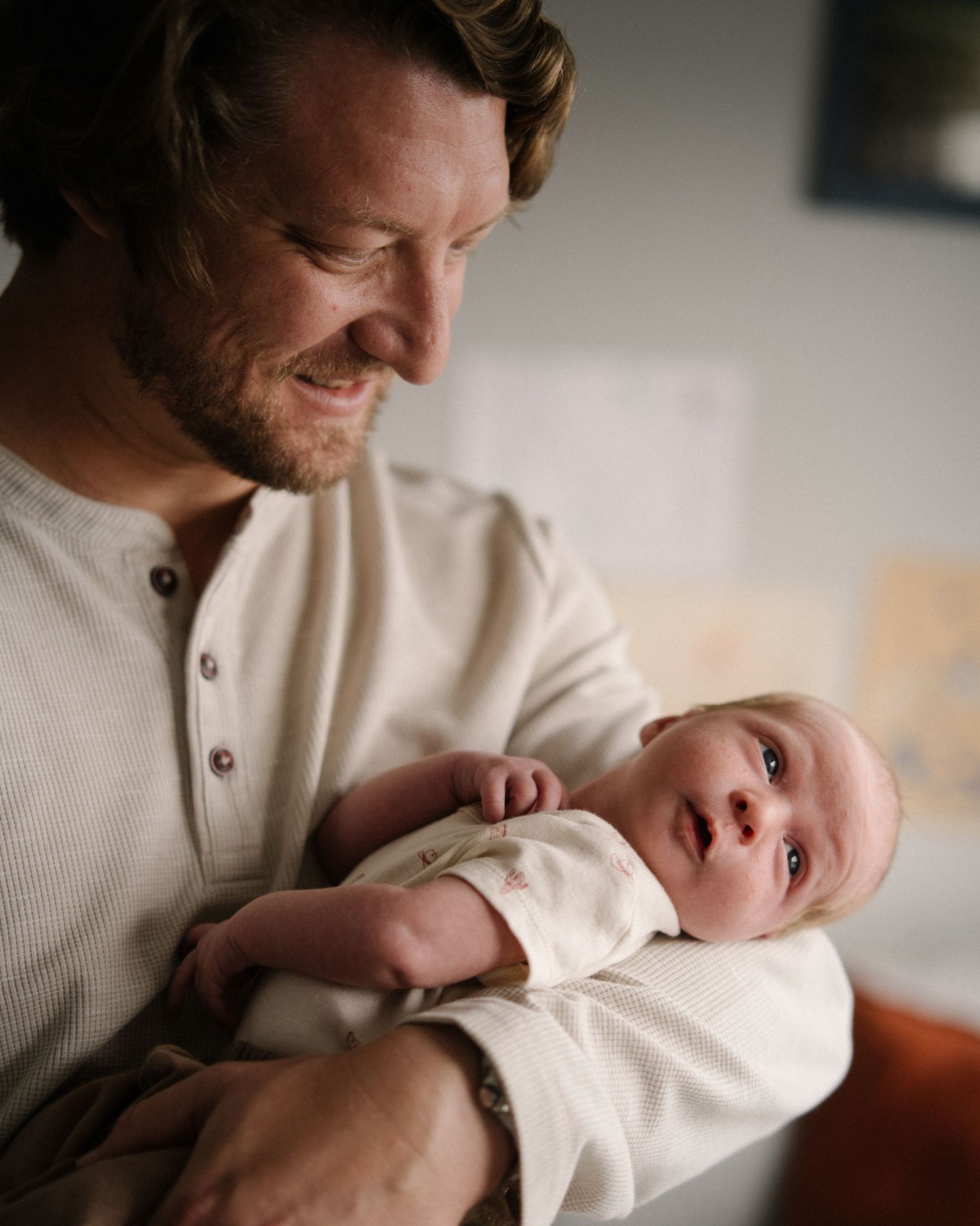 A tender moment between a parent and baby both wearing cream colored clothing while relaxing at home.