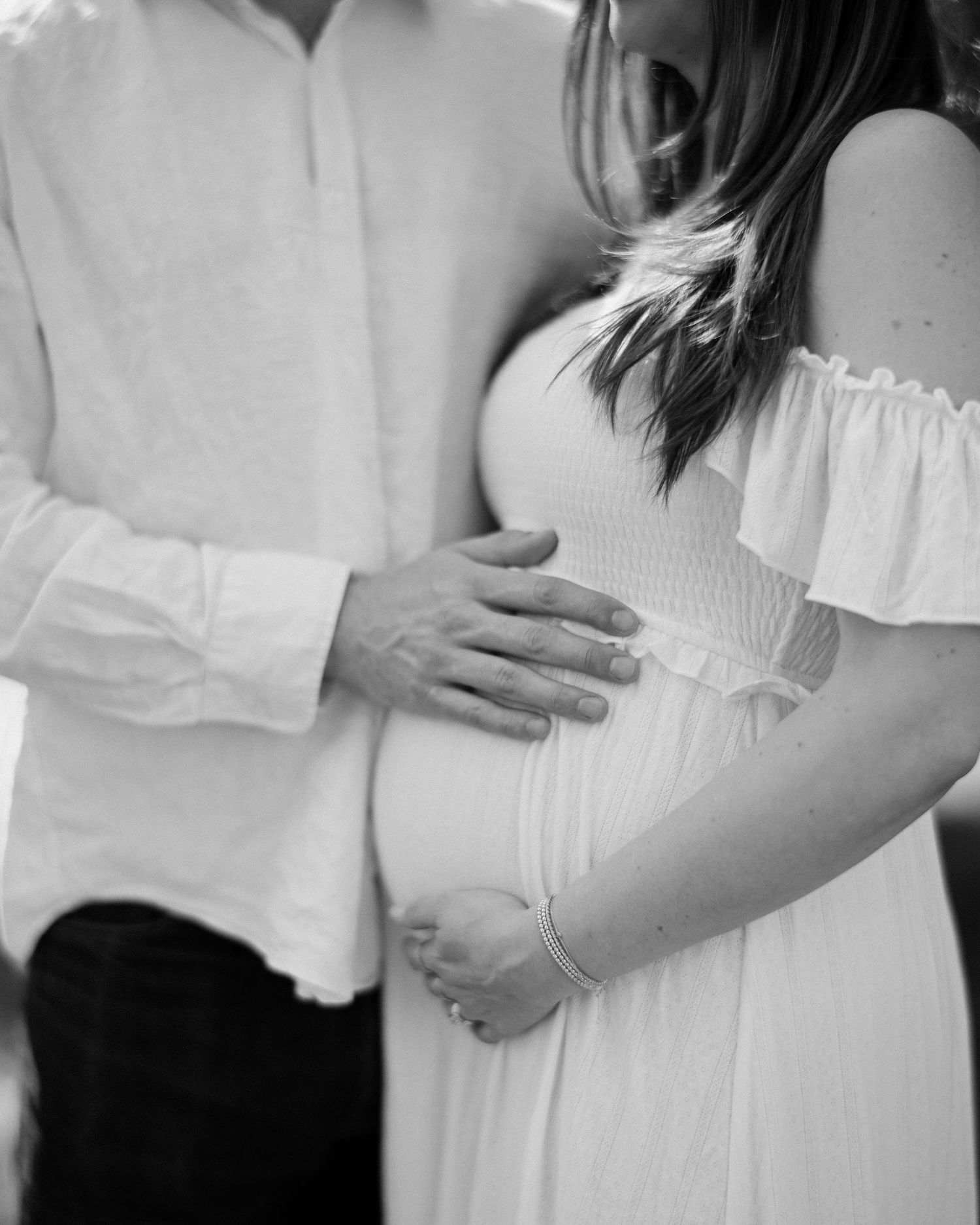 A series of black and white maternity photos showing a pregnant woman in white clothing embracing her baby bump.