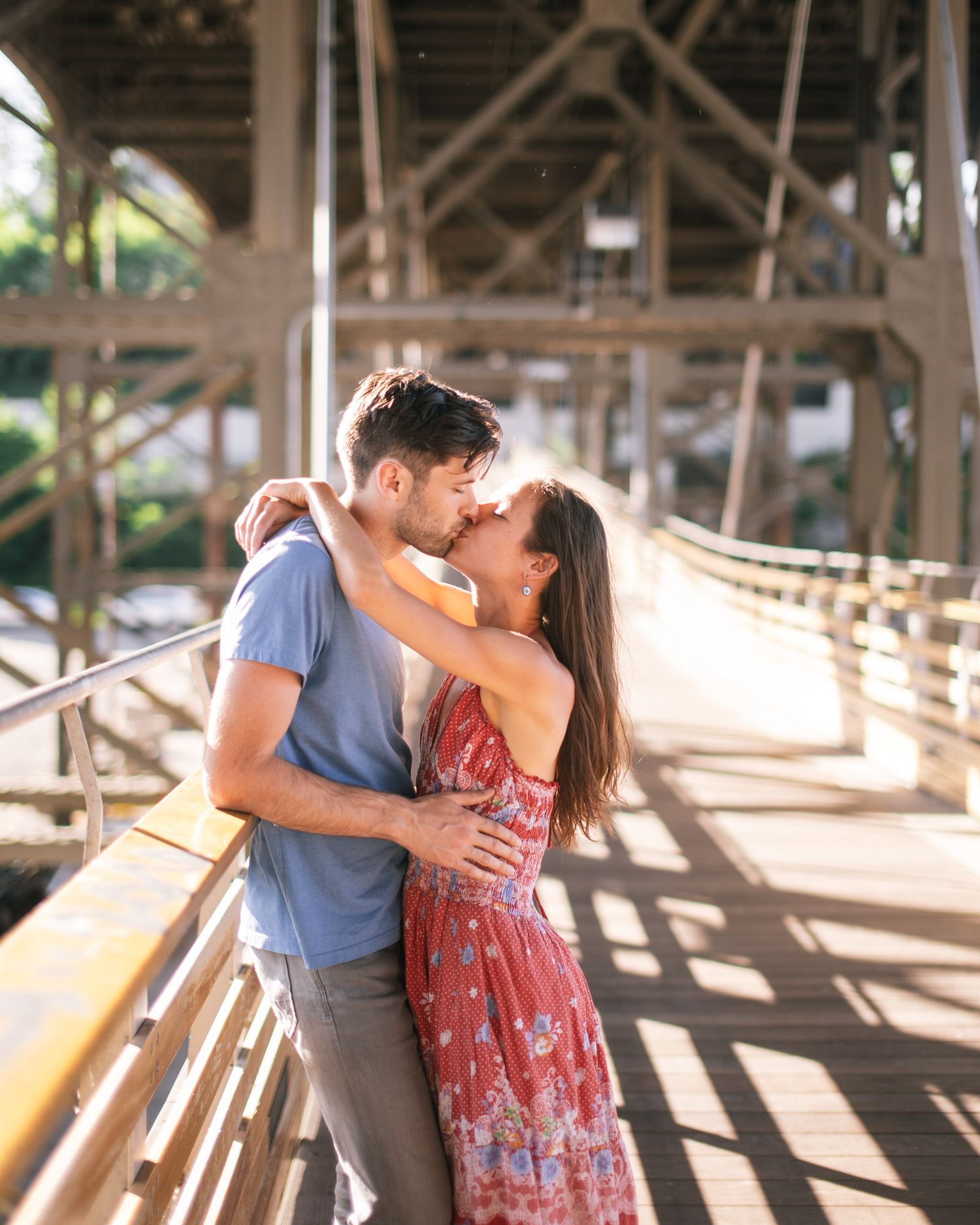 Romantic couple embracing on a wooden bridge in warm sunlight.