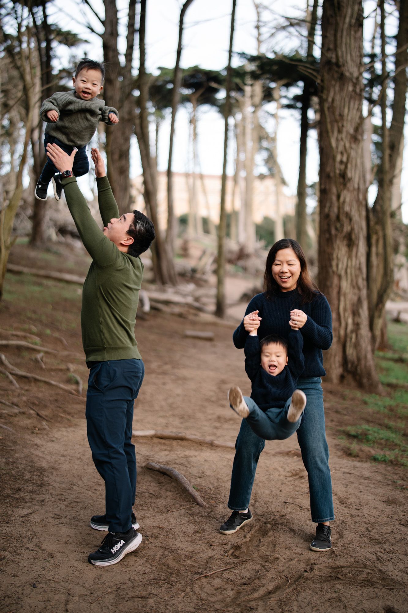 A family enjoys playful moments together on a dirt trail in a wooded area during an outdoor adventure.